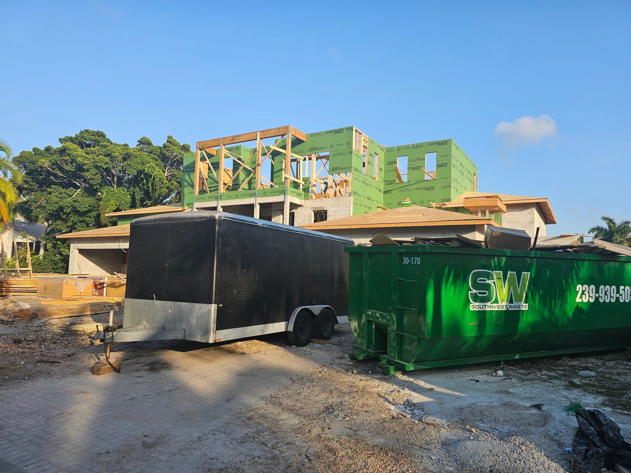 Construction site with partially built house, green dumpster, and black trailer. PrimeCorebuilders