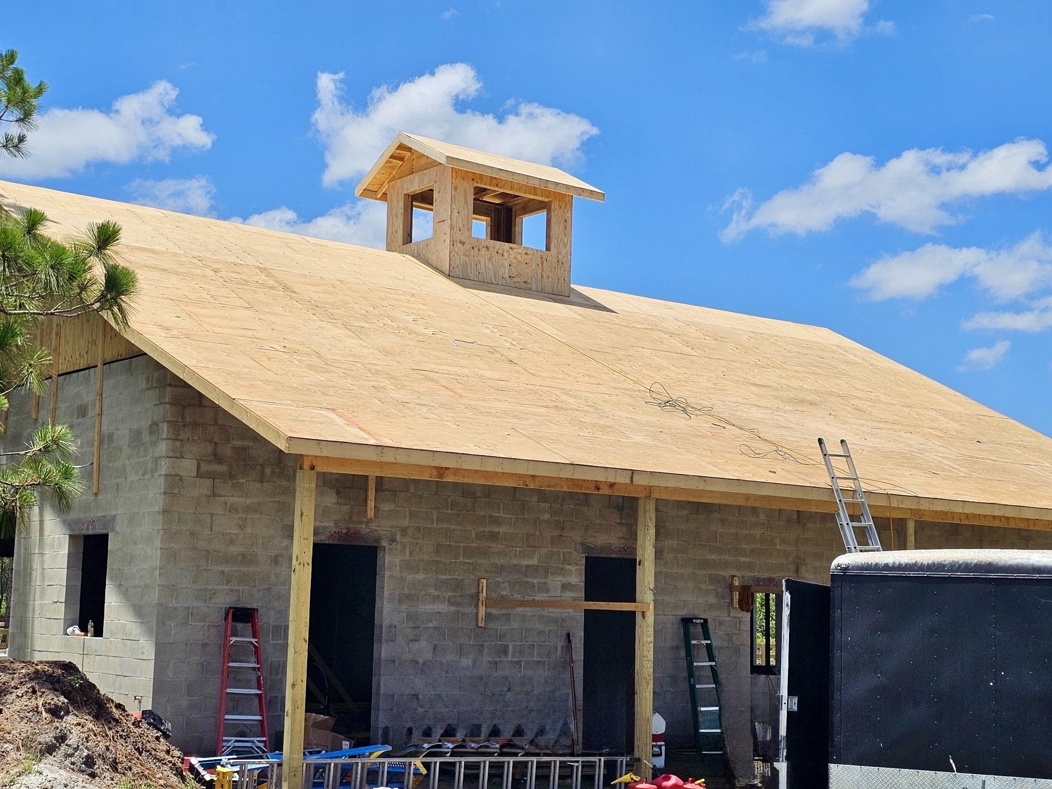 Under-construction building with unfinished roof and cupola, concrete block walls, ladders, and tools visible.