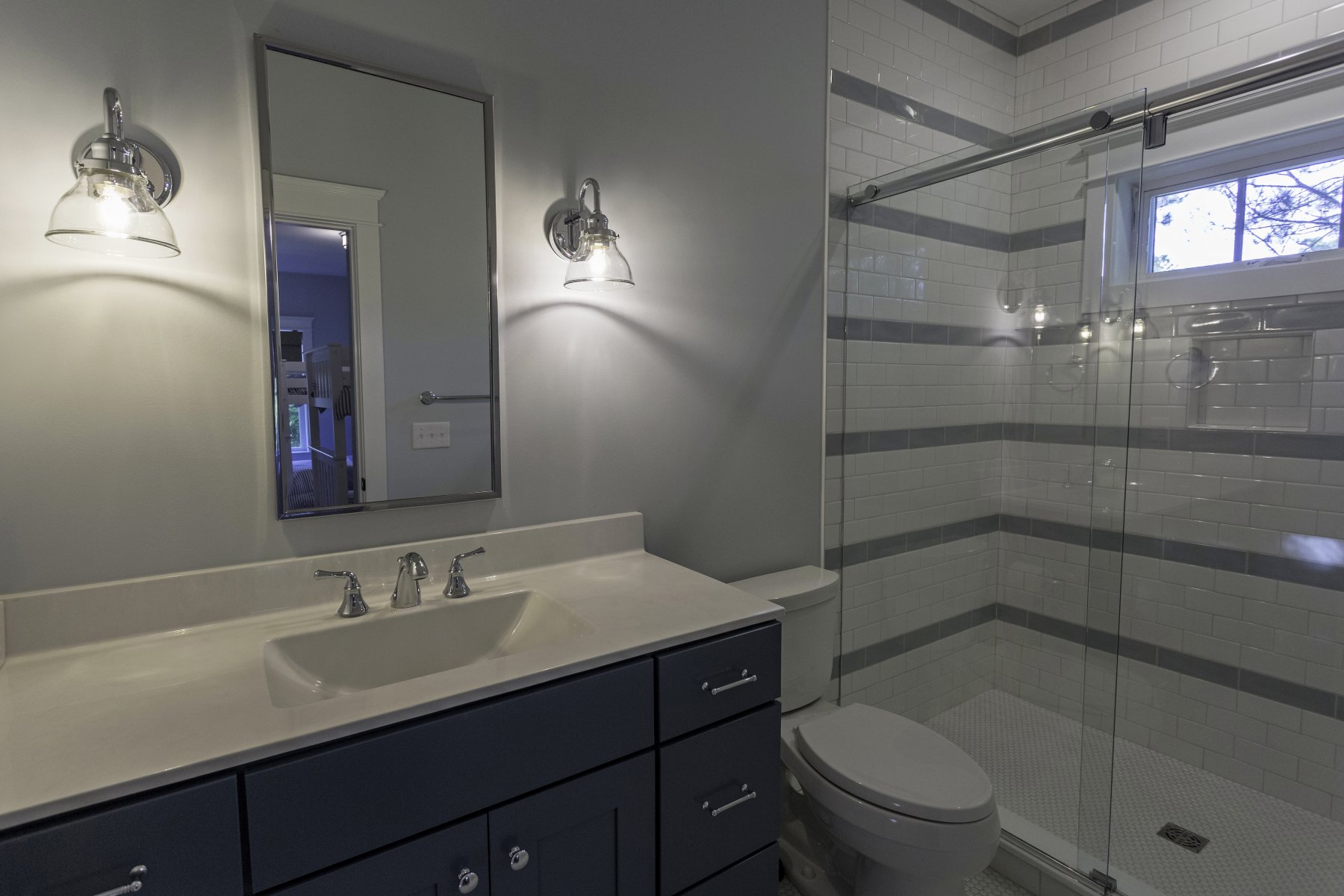Modern bathroom with single sink vanity, chrome faucet, mirror, two wall-mounted lights, toilet, and glass-enclosed shower.