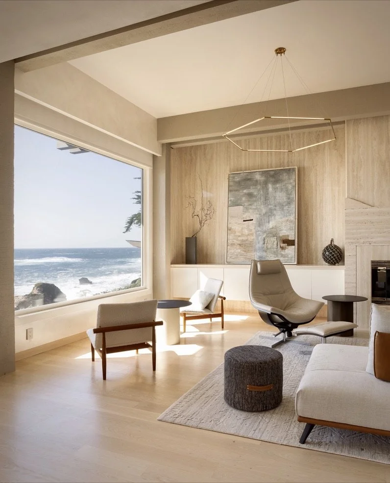 Modern living room with ocean view, featuring contemporary furniture, large window, light wood flooring, abstract art, and a geometric ceiling light.