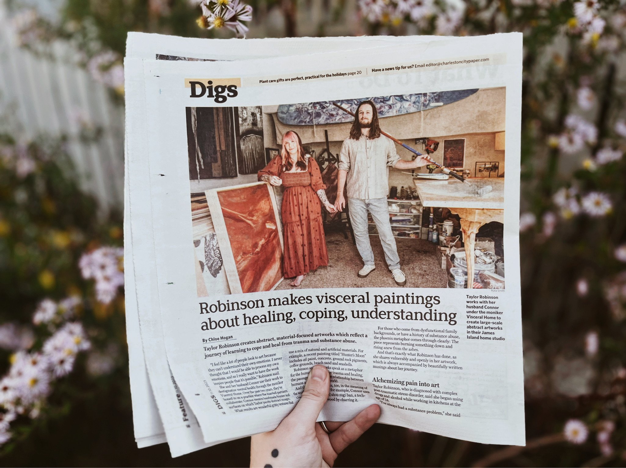 Newspaper section titled 'Digs' showing two people holding hands in an art studio with paintings. Headline reads 'Robinson makes visceral paintings about healing, coping, understanding.'