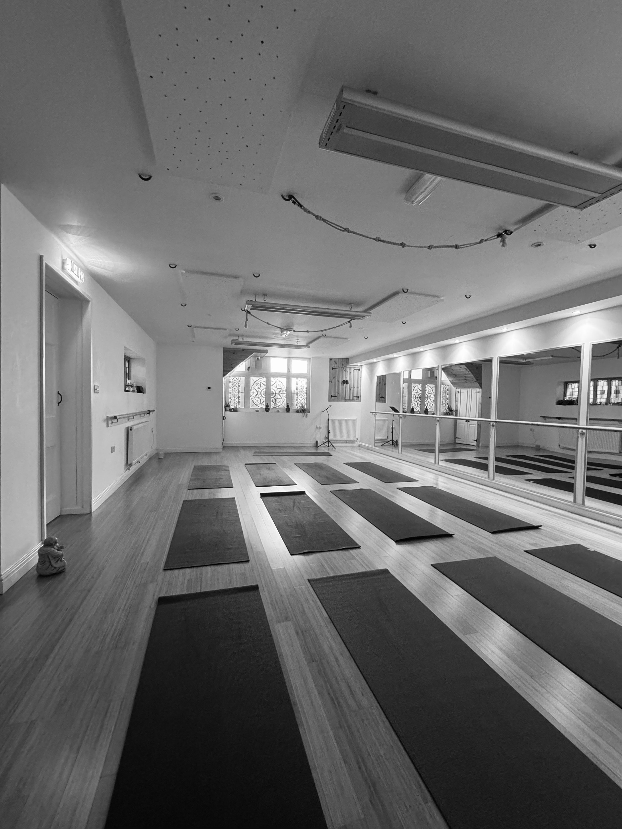 Yoga studio with arranged mats on wooden floor, mirrored wall, and ceiling lights.