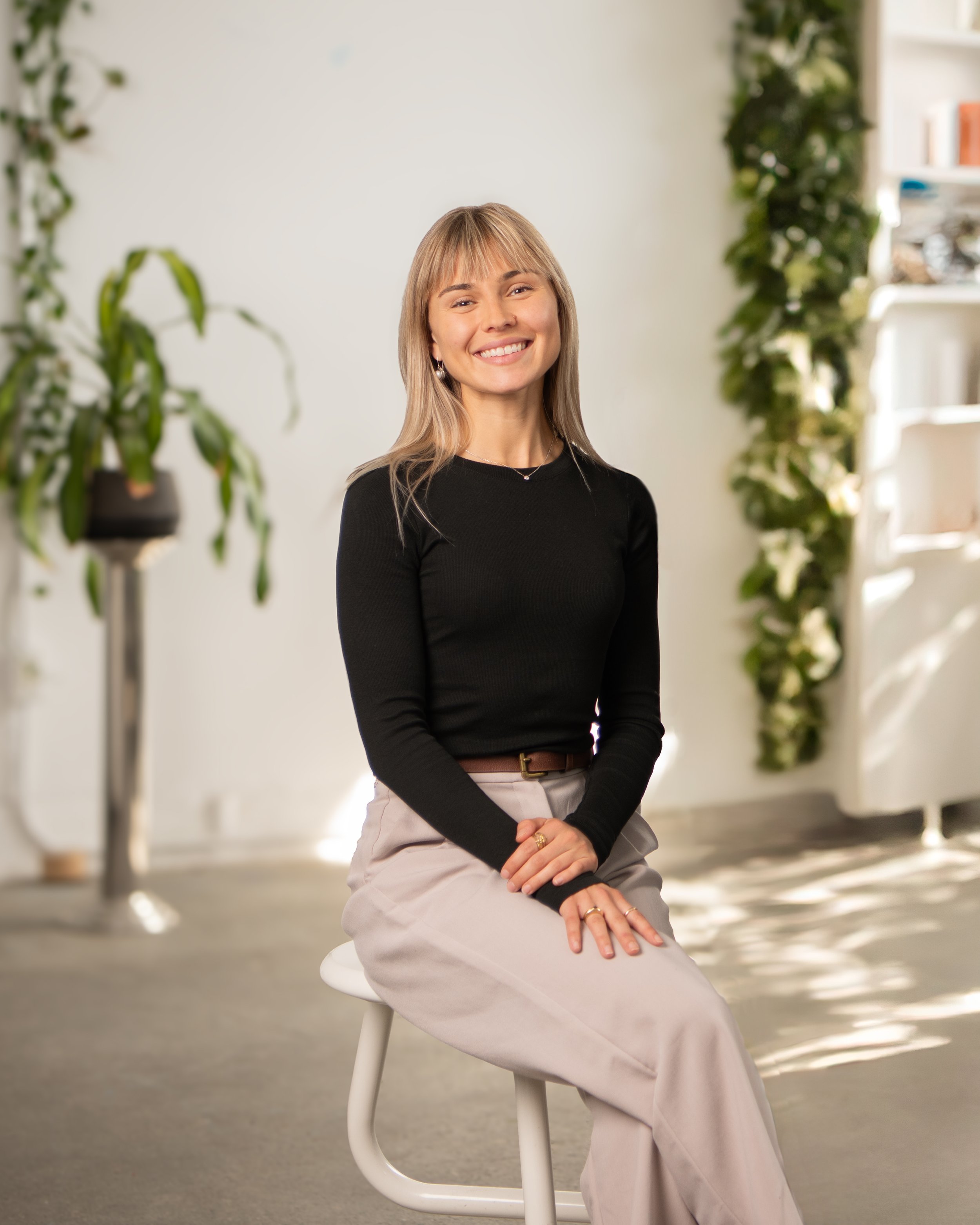Ilona Lafitte, Directrice des opérations , assise sur une chaise blanche dans un intérieur lumineux avec des plantes vertes en arrière-plan.