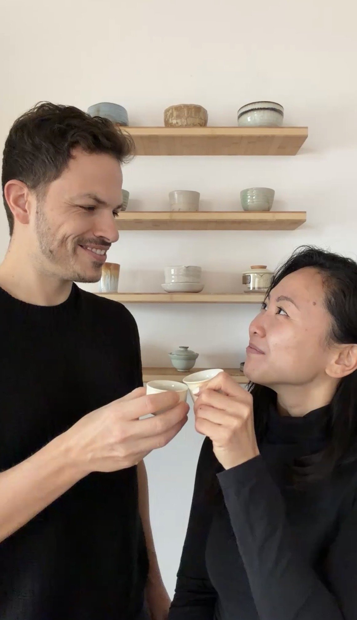 Zwei Menschen stoßen mit kleinen Tassen an, während sie sich ansehen und lachen.