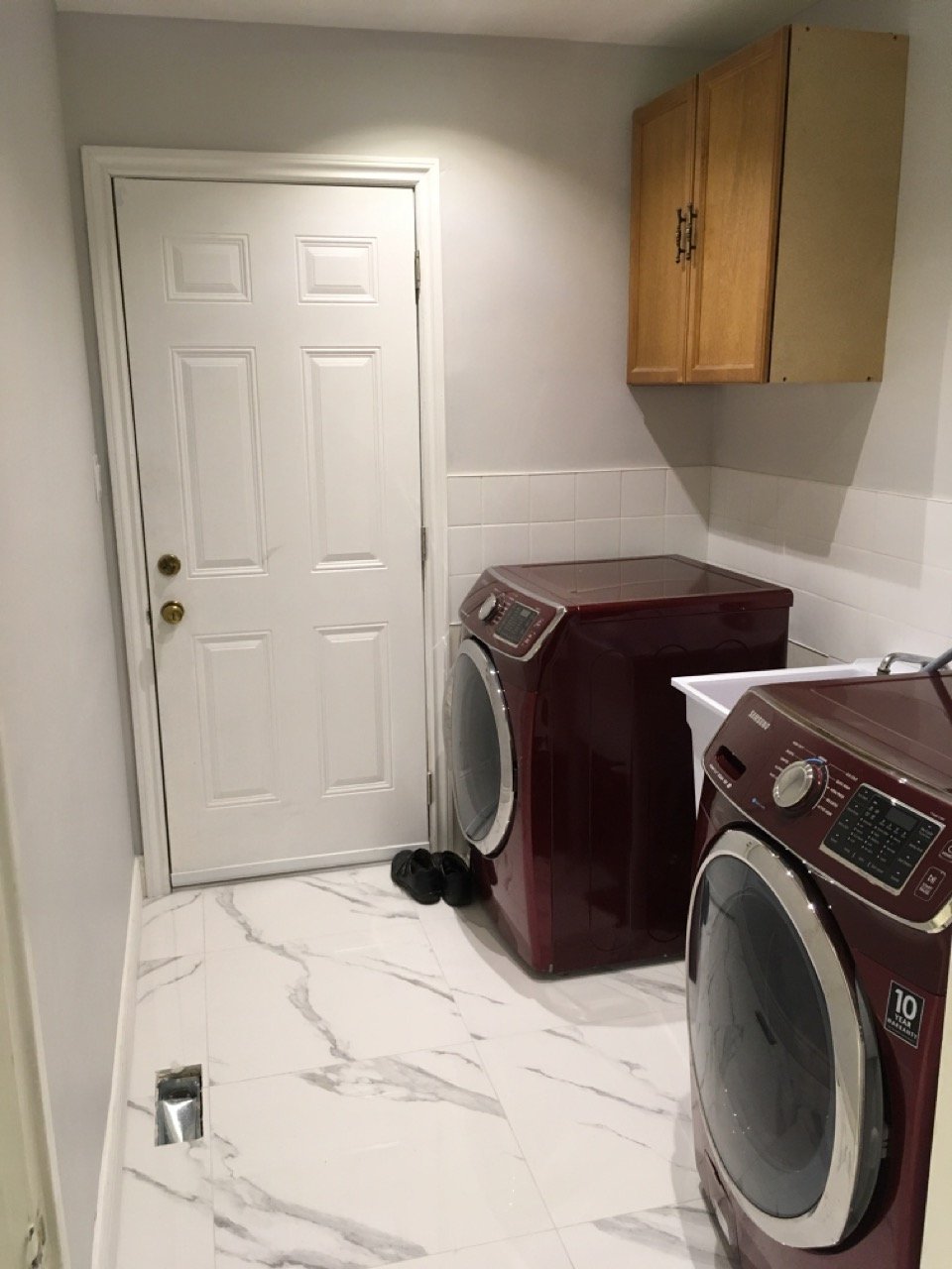 Laundry room with red washer and dryer, marble tile floor, white wall, wooden cabinets, white door