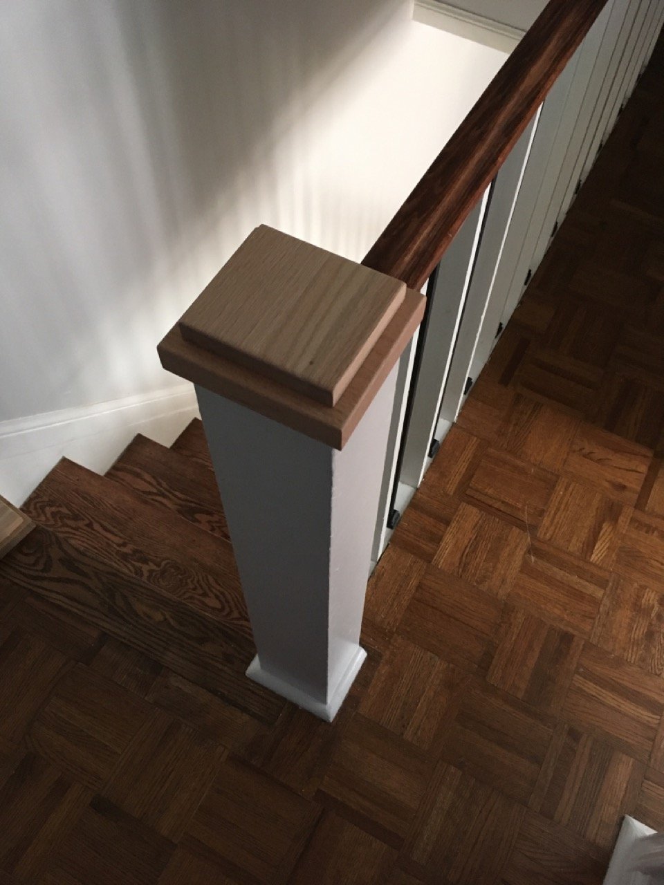 View of a staircase with wooden railing, parquet floor, and a square newel post.