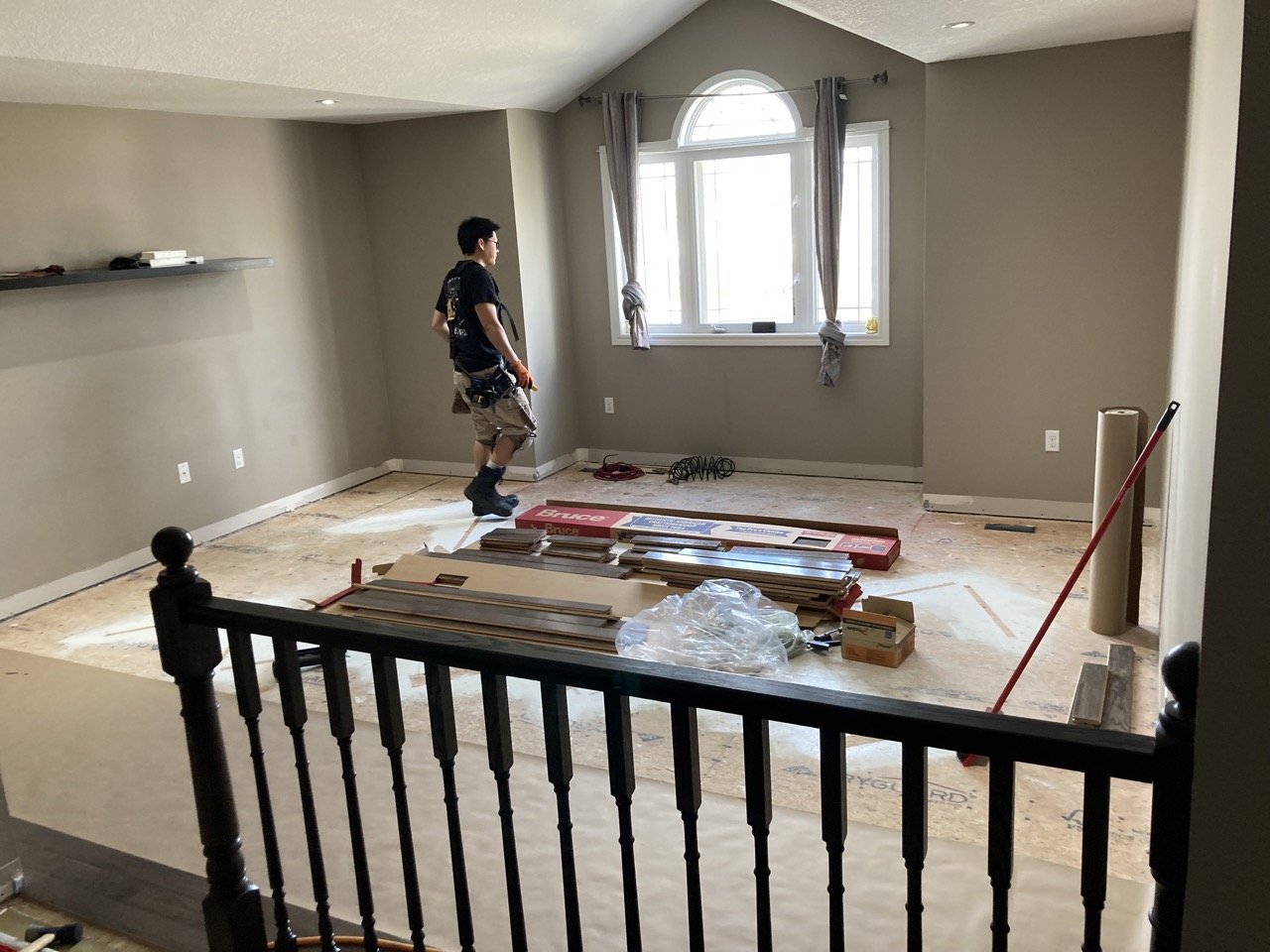 A person preparing a room for flooring installation with tools and materials scattered on the floor.