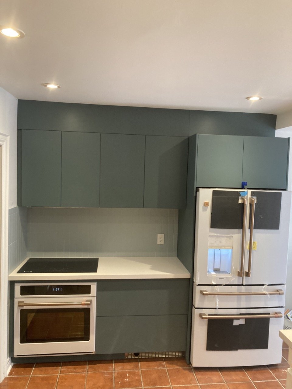 Modern kitchen with gray cabinets, built-in oven, induction cooktop, and white refrigerator. Tile flooring and recessed lighting are visible.
