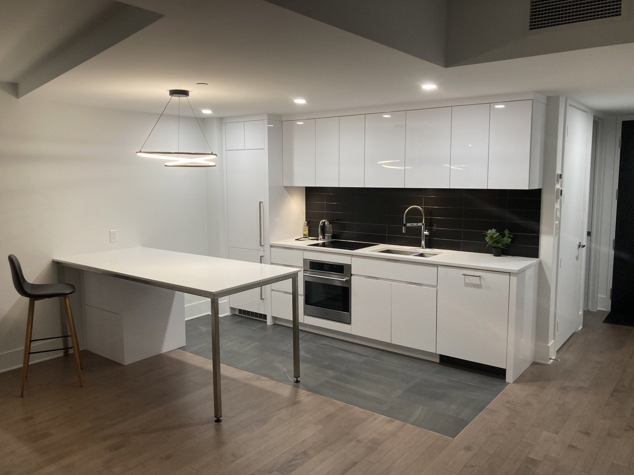 Modern kitchen with white cabinets, black backsplash, built-in oven, and minimalist island with high chair.