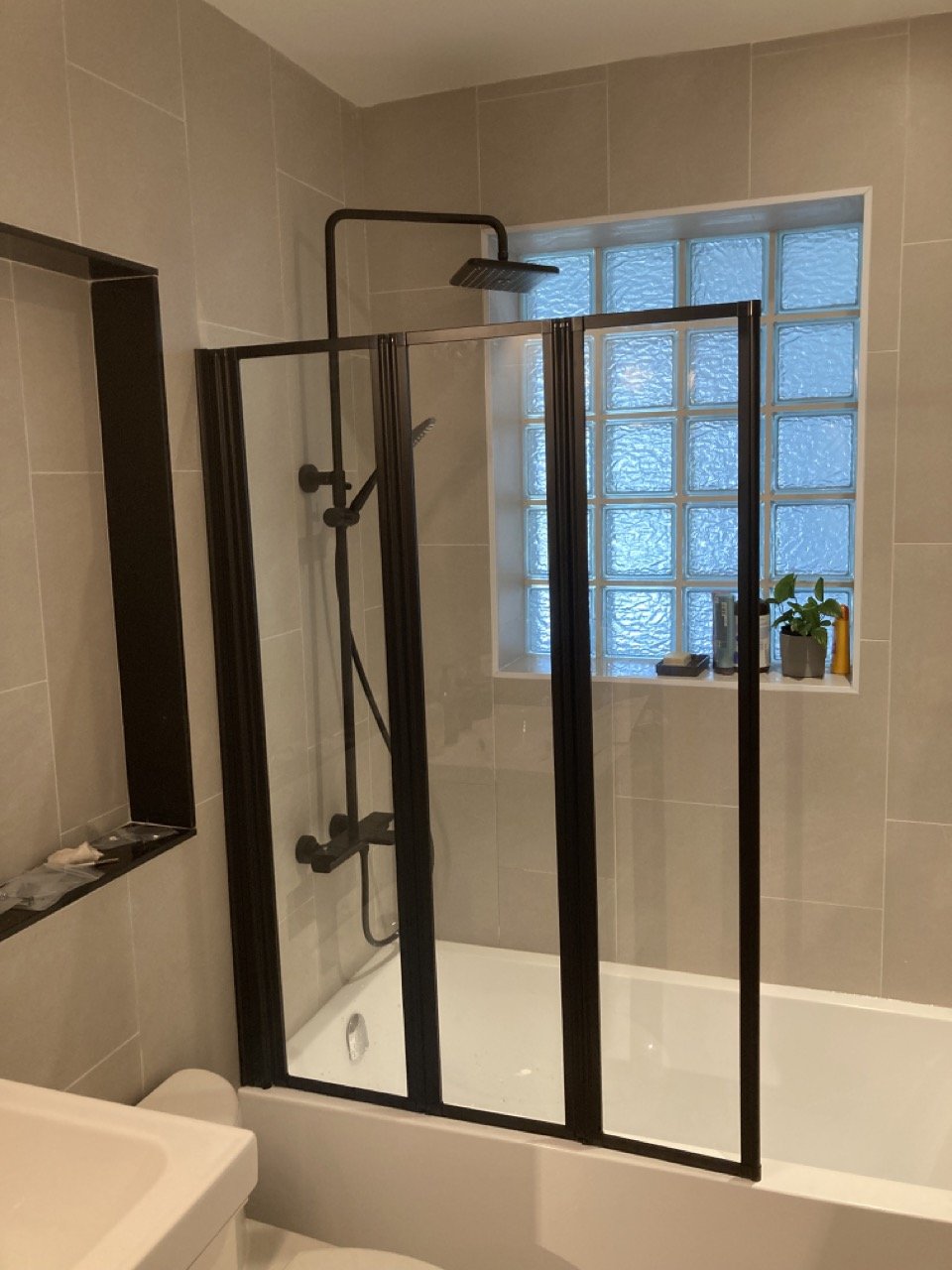 Modern bathroom with glass block window, shower with black frame and fixtures, and gray tiles.