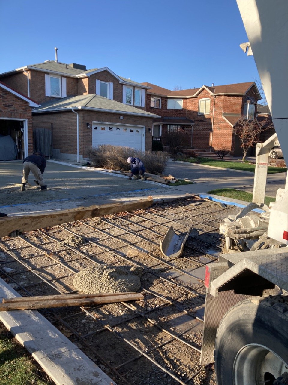 Construction workers pouring concrete on a driveway of a suburban house during renovation.