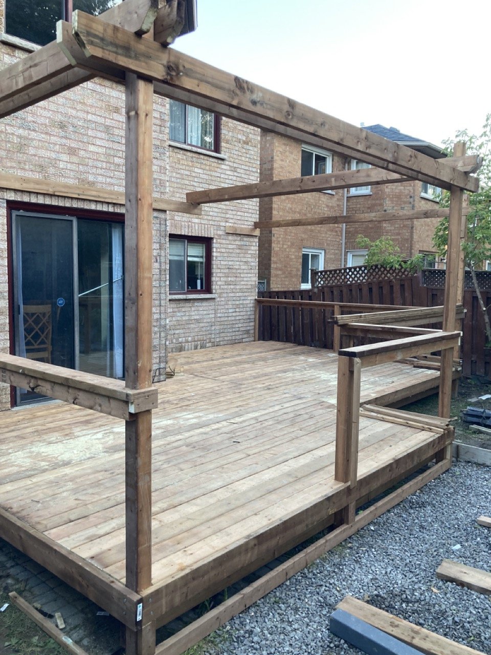 Wooden deck under construction with framing for a pergola, adjacent to a brick house.