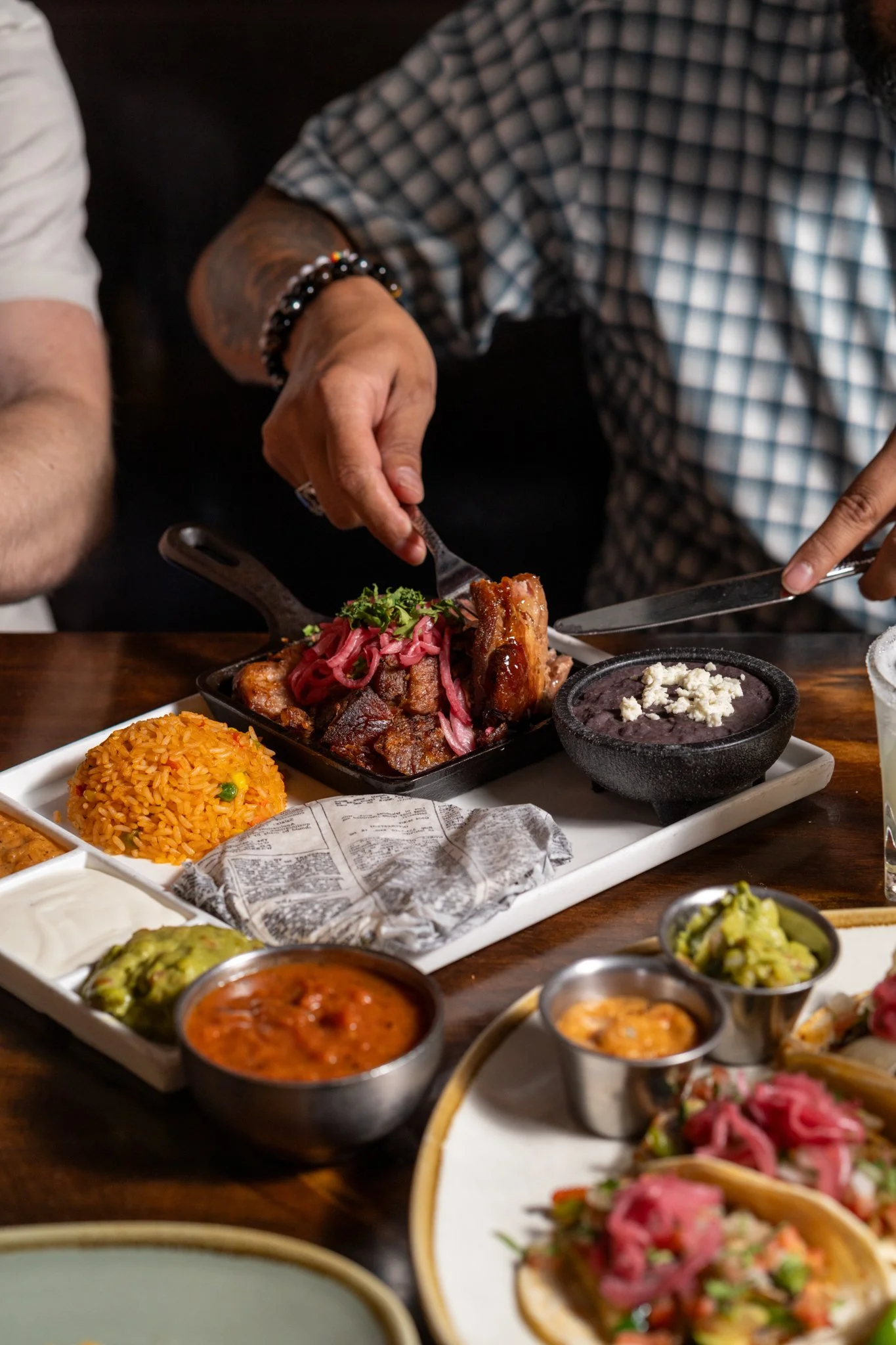 Food photography for Richard Sandoval restaurant Venga Venga in Aspen, COPerson serving ribs with pickled onions, surrounded by Mexican dishes including rice, salsa, guacamole, and tacos.