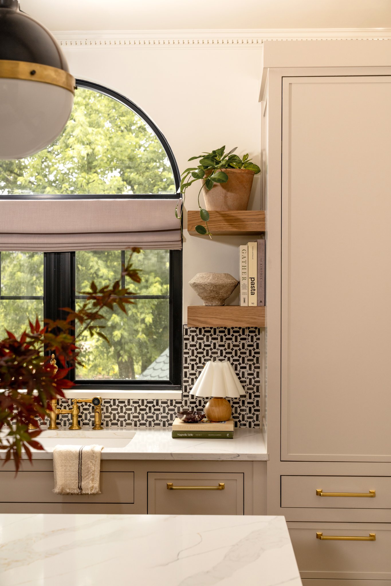 Kitchen with a window, a small lamp, books, a potted plant, and a black and white tiled backsplash.
