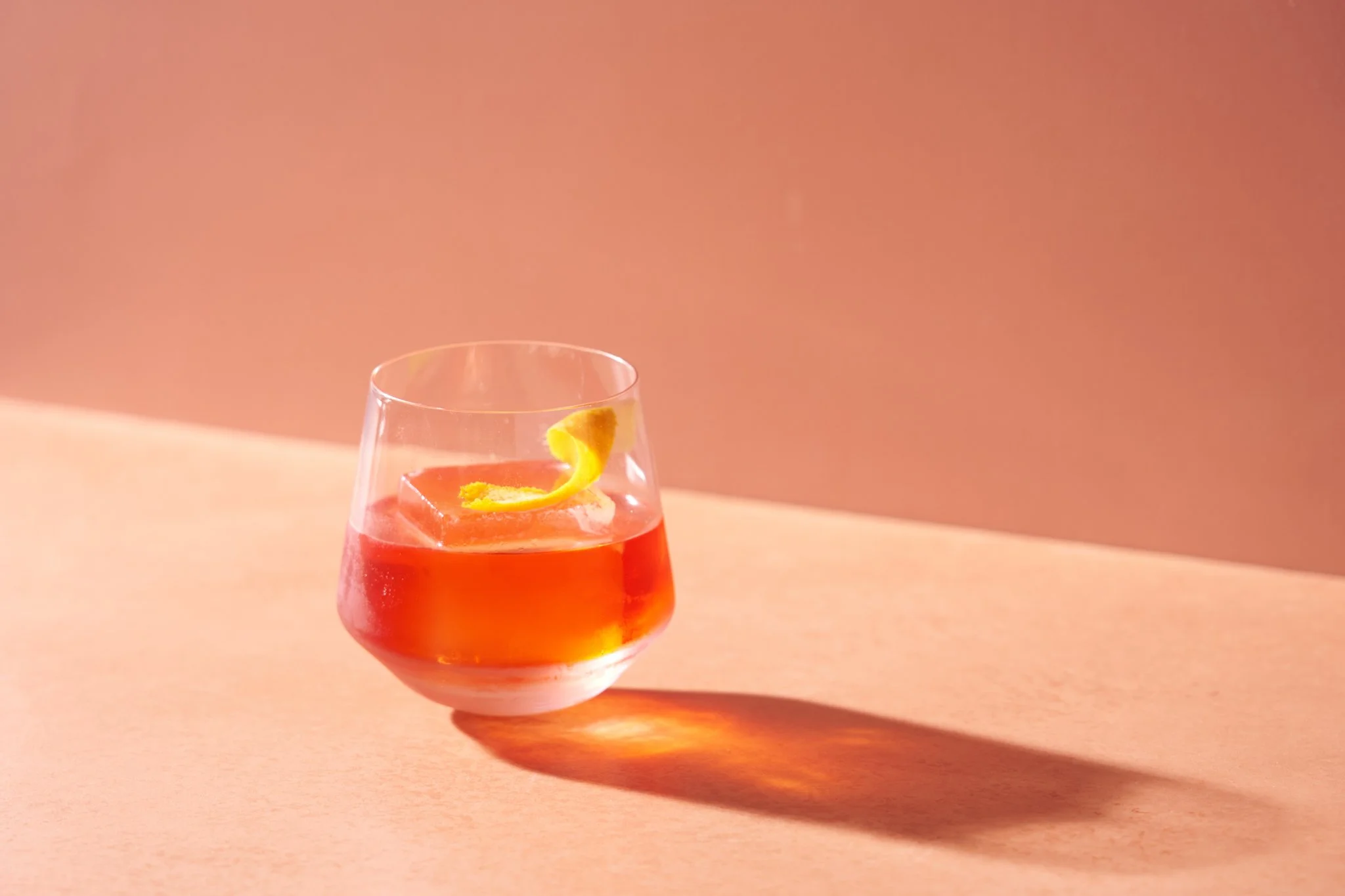 Beverage photography  for Richard Sandoval Hospitality featuring A glass of pink cocktail with ice and a lemon twist on a pink surface with a pink background.