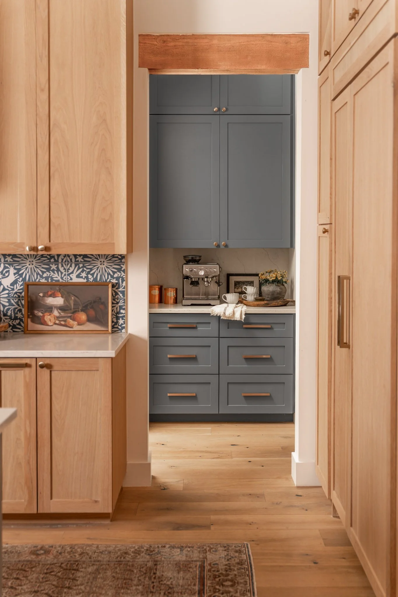 Kitchen with wooden cabinetry, a blue built-in cabinet area, and a coffee machine on the counter, decorated with framed photos, cups, and flowers.