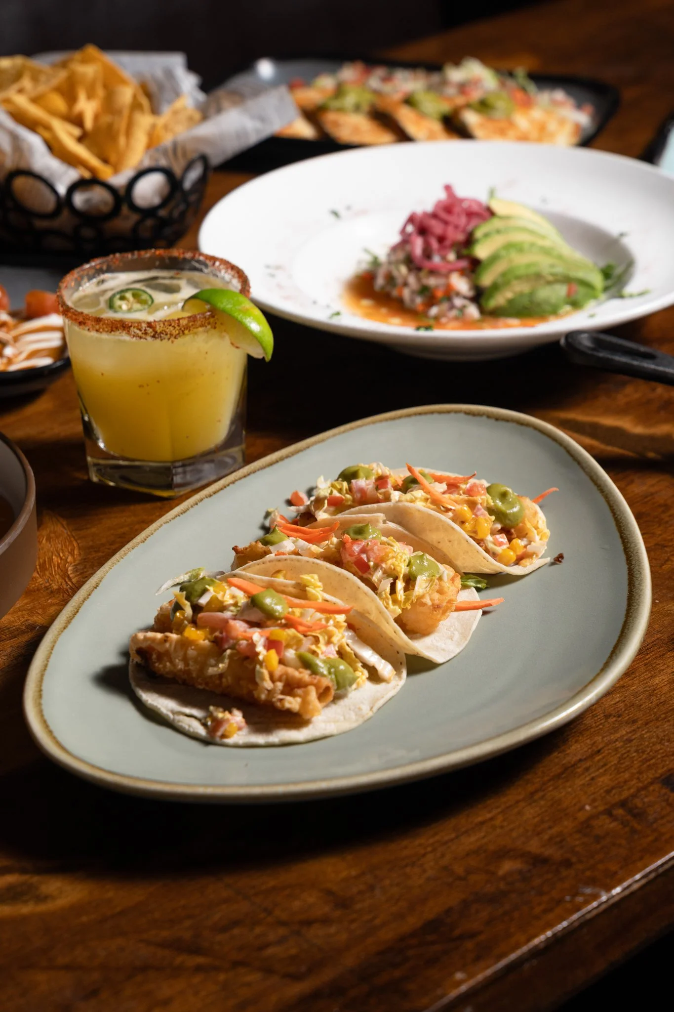 	
Food photography for Richard Sandoval restaurant Venga Venga in Aspen, CO  Three fish tacos with lettuce, tomatoes, and green peppers on a light green plate, a margarita with lime on the rim, and various Mexican dishes on a wooden table.