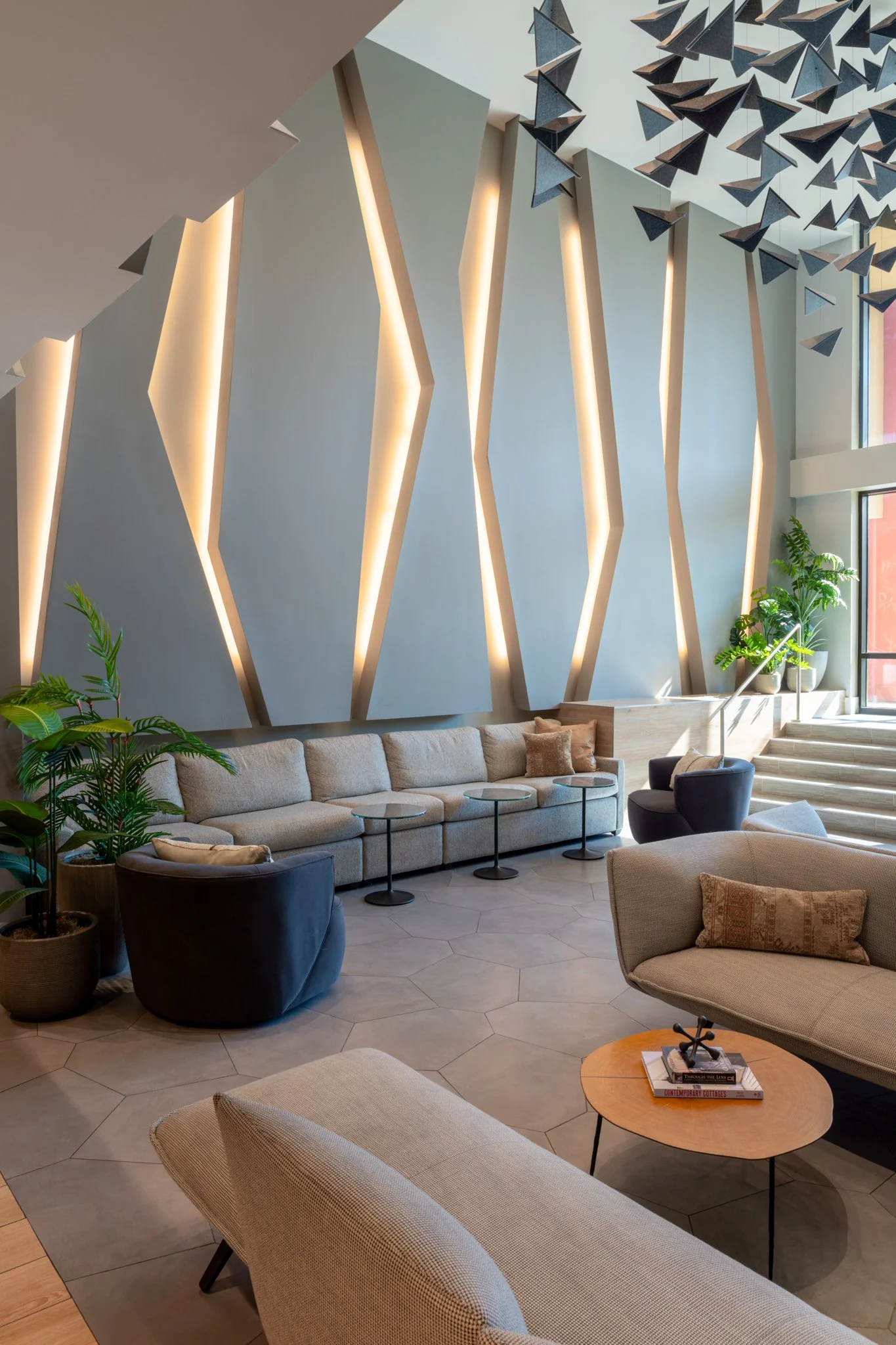 Architectural Photography featuring modern apartment lobby or lounge area with beige and black sofas, potted plants, geometric wall design with warm lighting, and decorative hanging art installation at the ceiling in Austin Texas