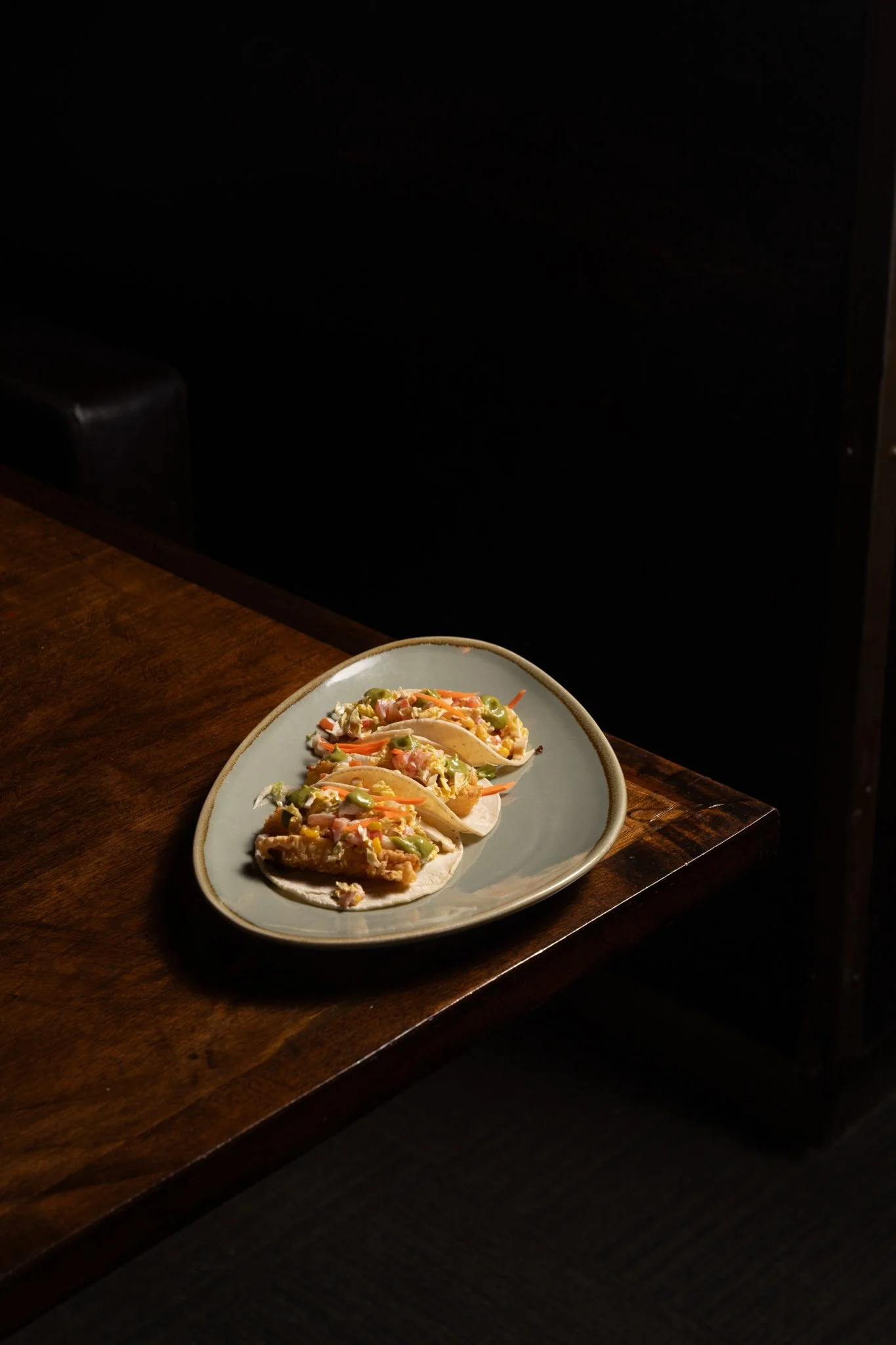 Food photography for Richard Sandoval Hospitality restaurant Venga Venga in Aspen, CO featuring Plate of three tacos with shredded vegetables on a wooden table in a dimly lit setting.