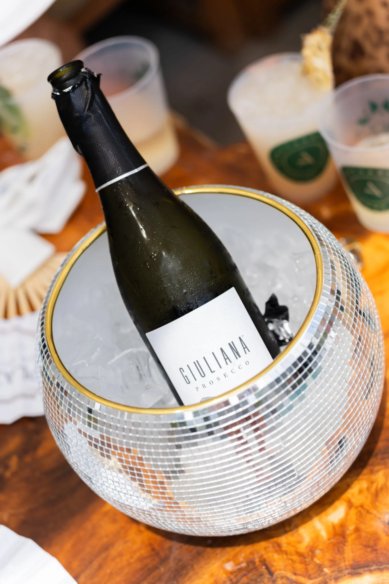 Commercial Photography with Plaza Hotel in San Antonio Texas featuring bottle of Giuliana Prosecco in a decorative ice bucket on a wooden table with empty glasses in the background.