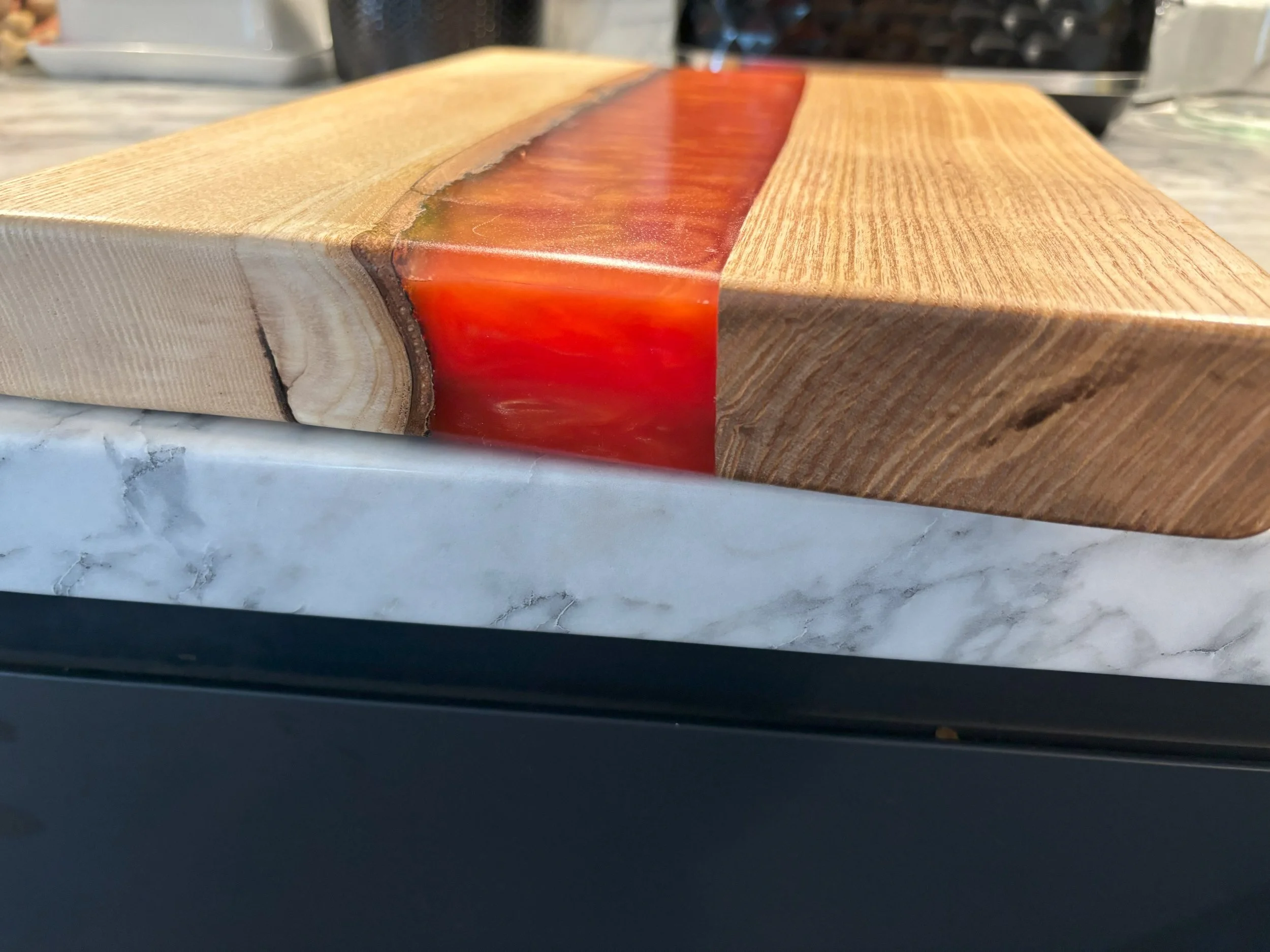 Wood and resin cutting board with red epoxy inlay on a marble countertop.