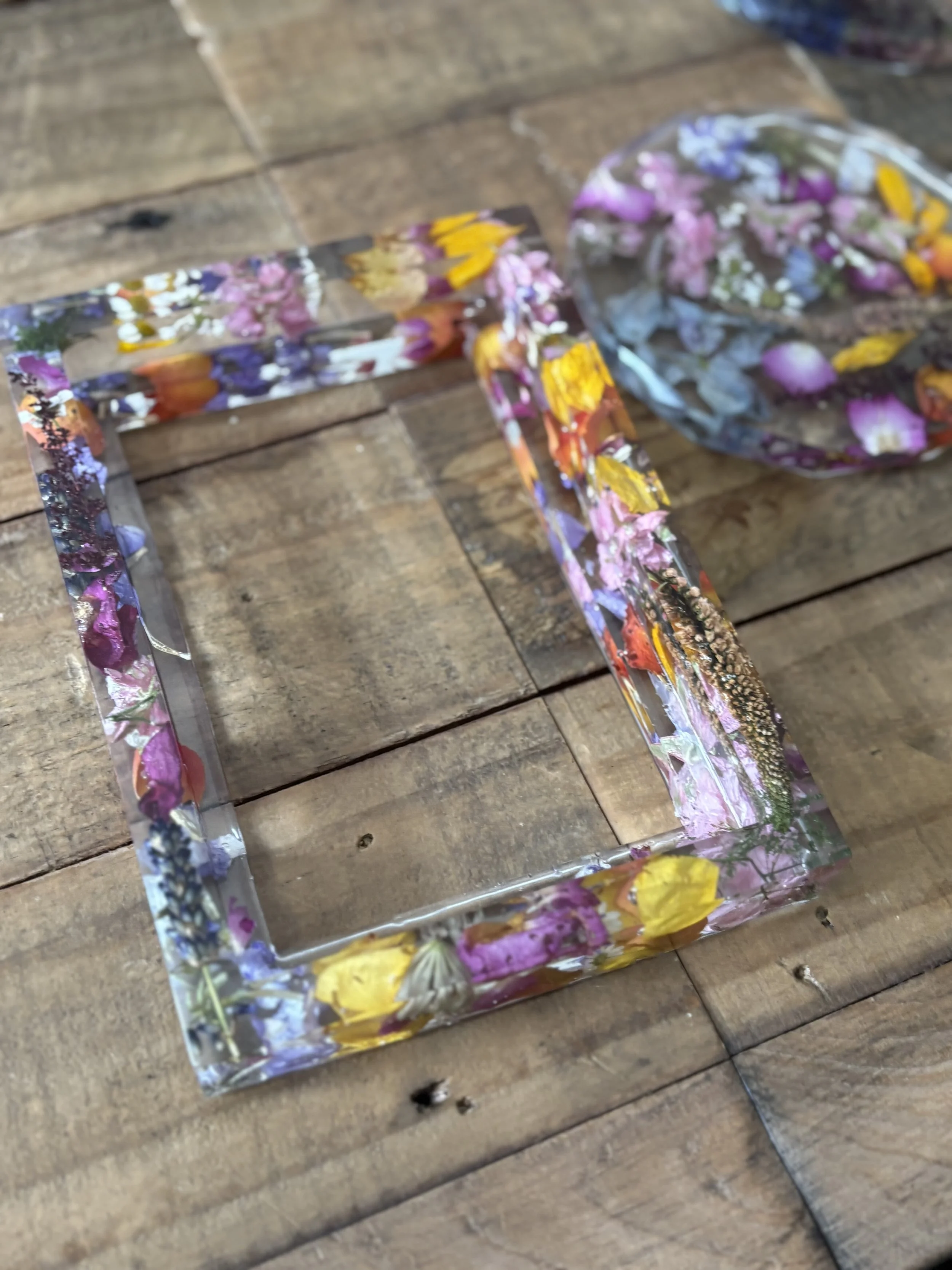 Transparent acrylic frame filled with colorful dried flower petals, placed on a wooden surface.
