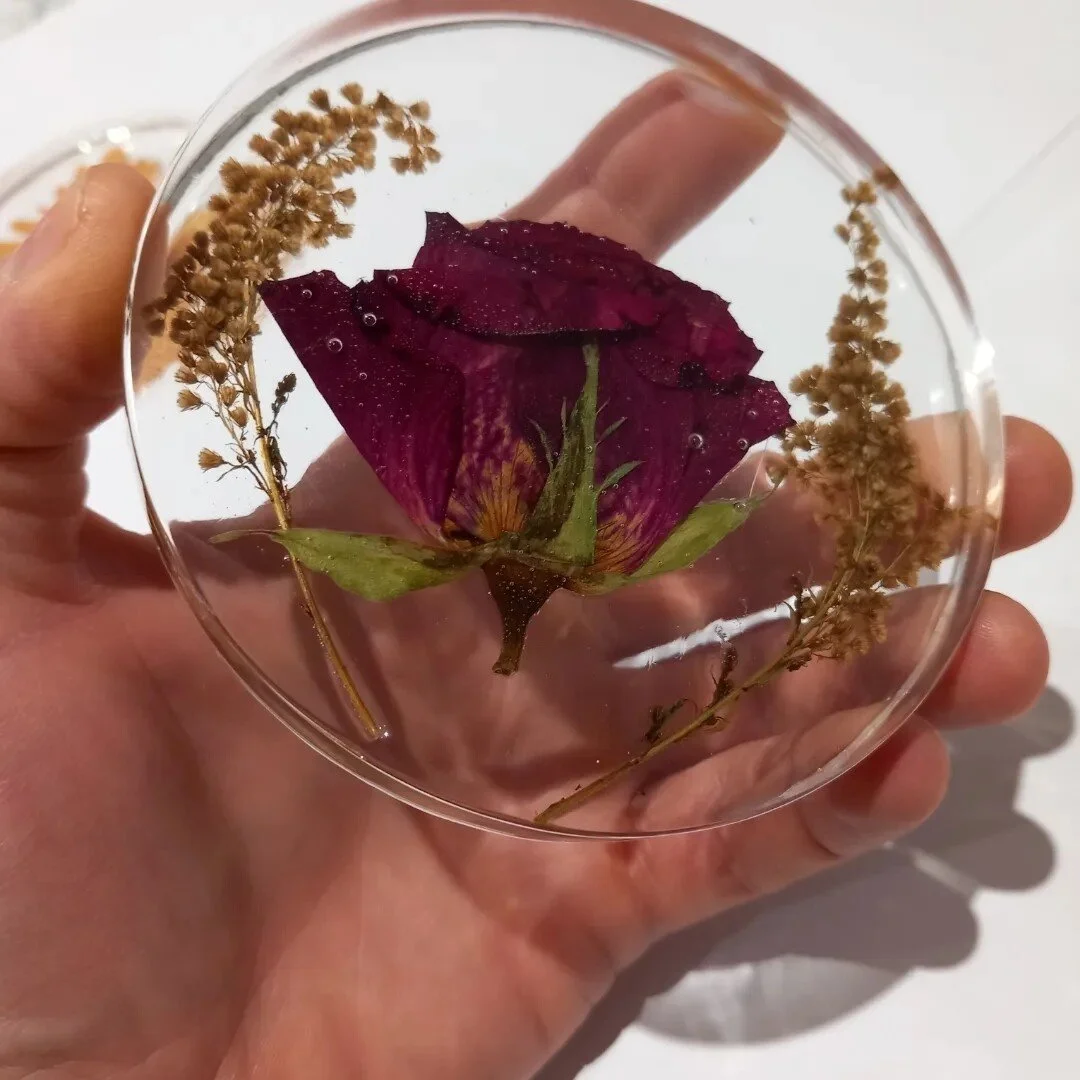 Transparent resin coaster with a preserved red rose and dried flowers held in a hand.