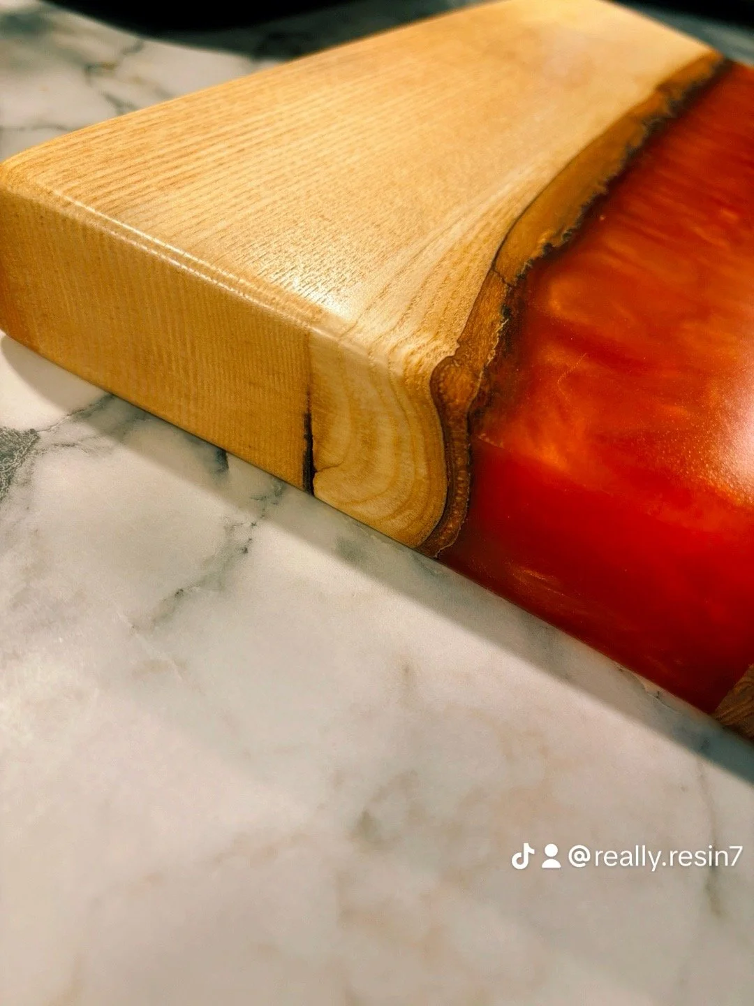 Close-up of a wooden block with a natural edge, resting on a white marble surface.