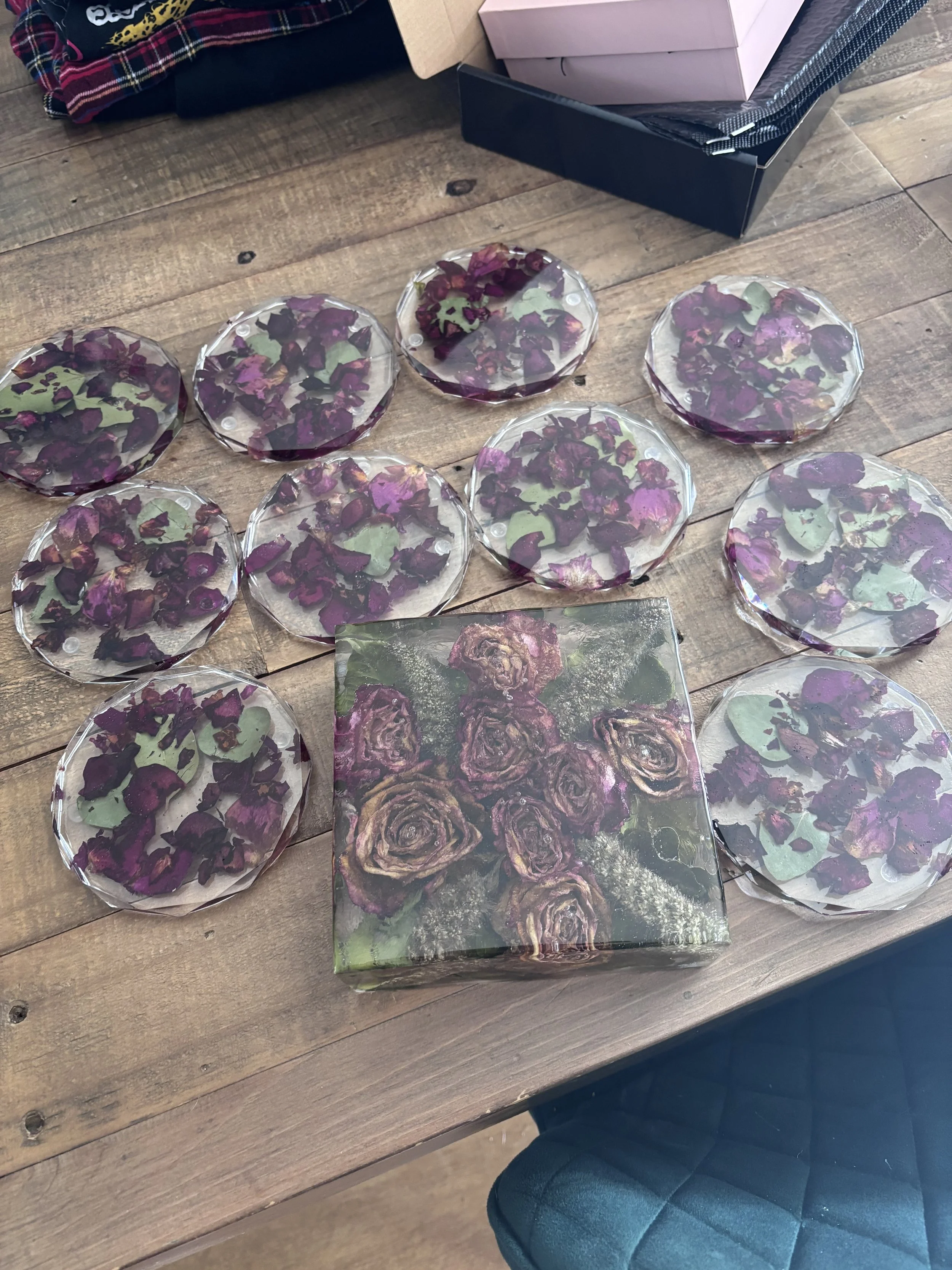 Set of ten glass coasters with purple floral designs and a box with an image of roses on the table.
