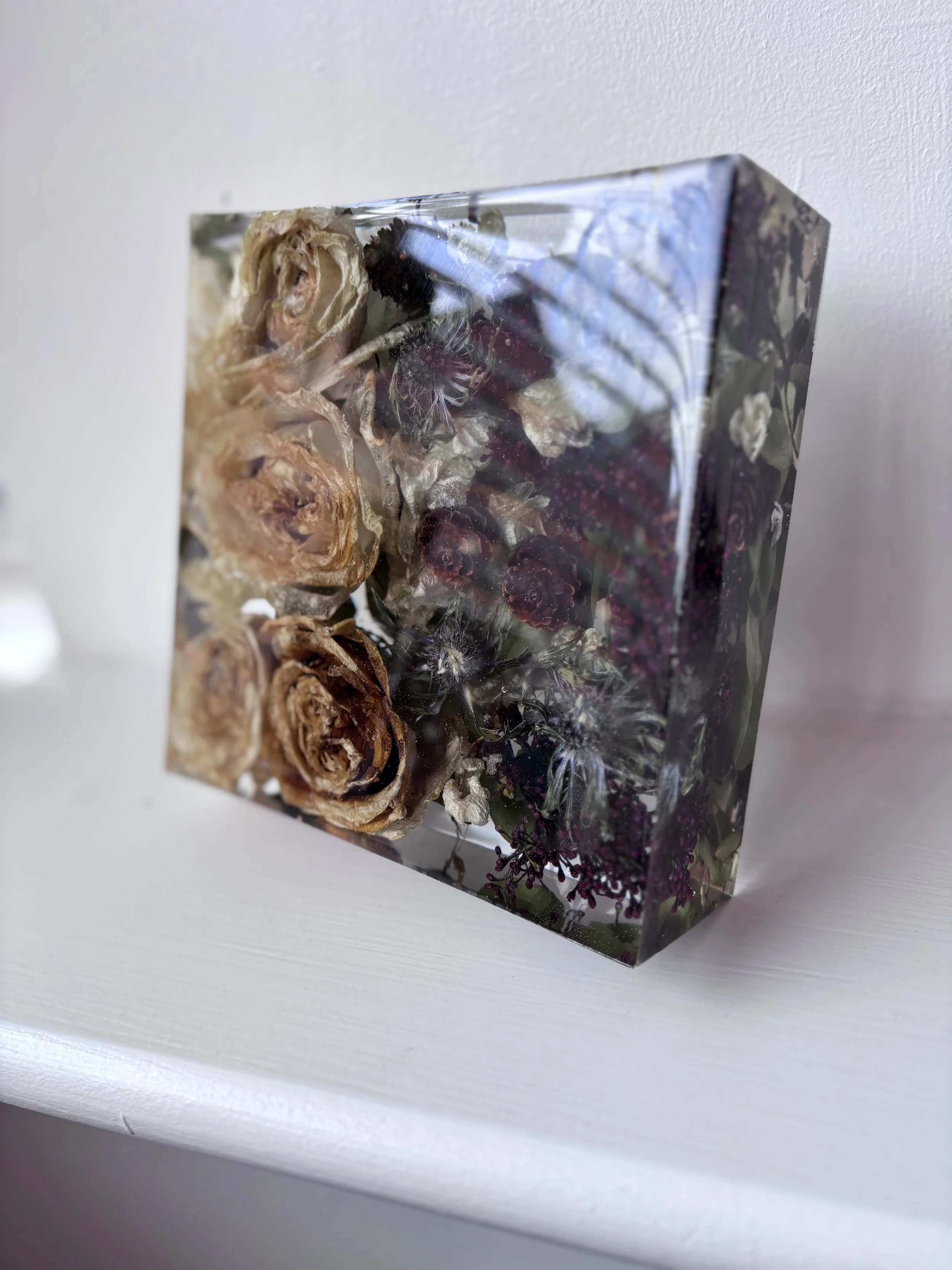 A transparent resin block containing dried flowers, including roses and other small flowers, mounted on a white surface.