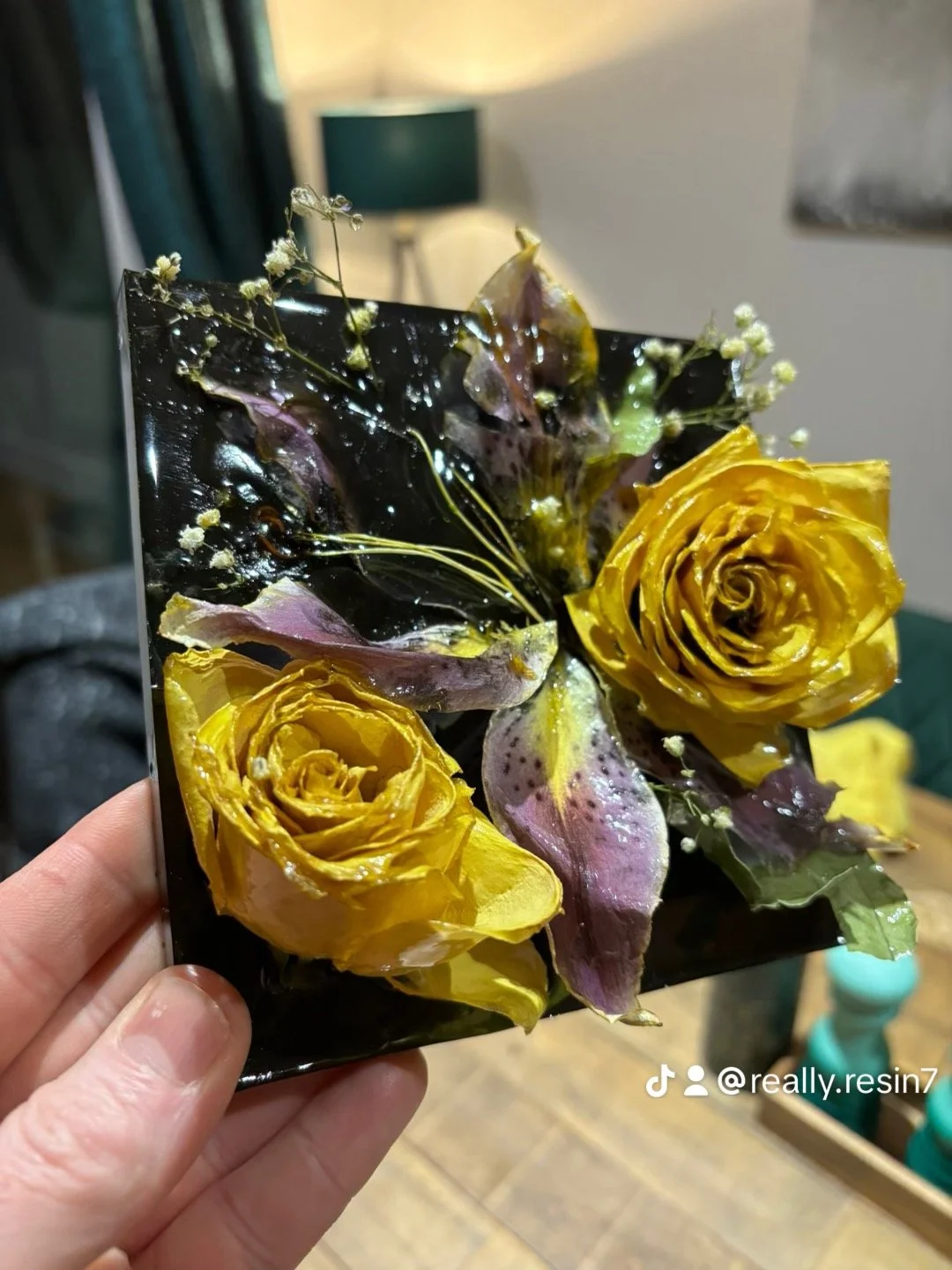 Resin art of yellow roses, purple leaves, and small white flowers in a black rectangular frame.