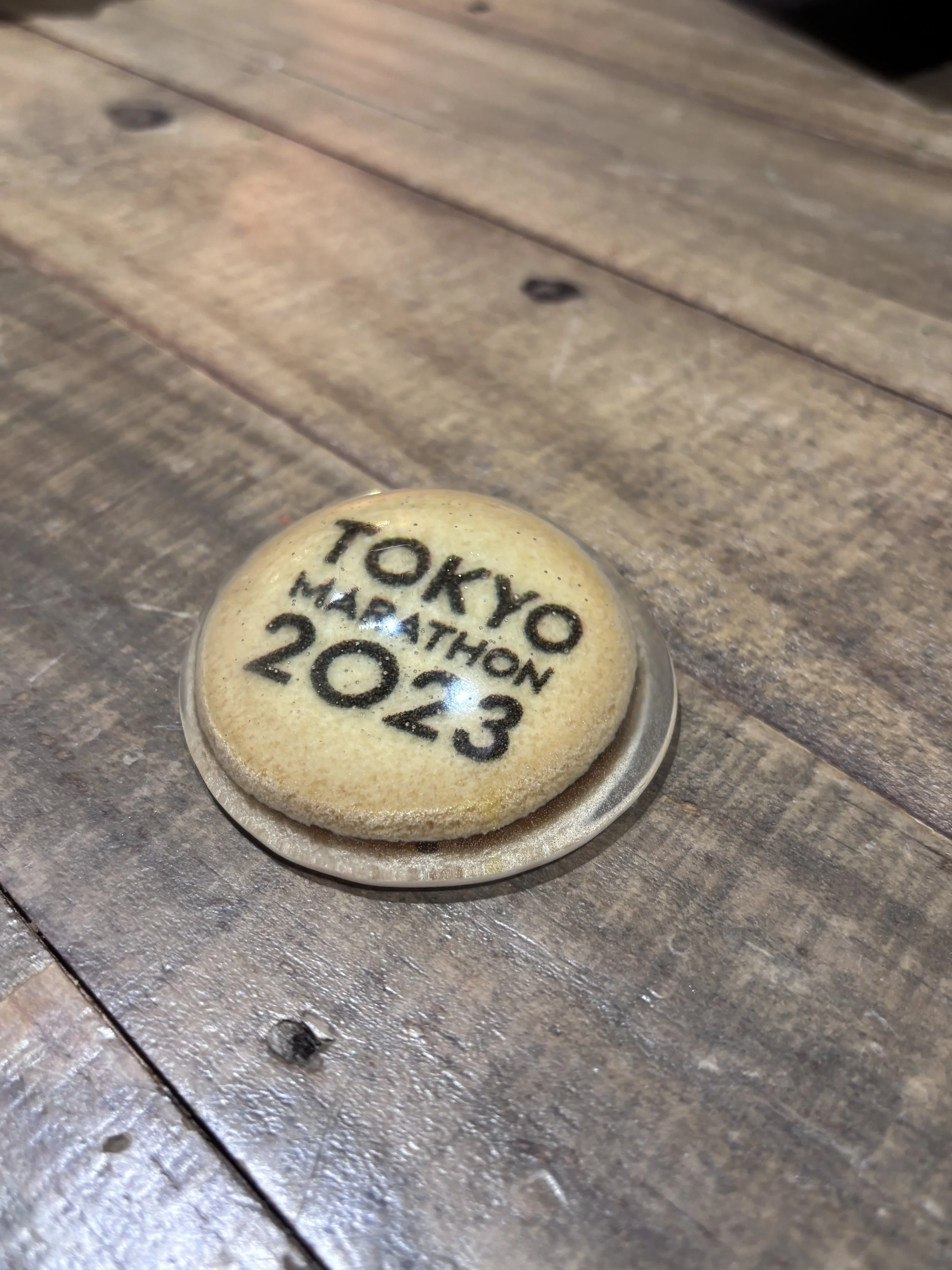 A round coaster with the text 'Tokyo Marathon 2023' printed on it, placed on a wooden surface.