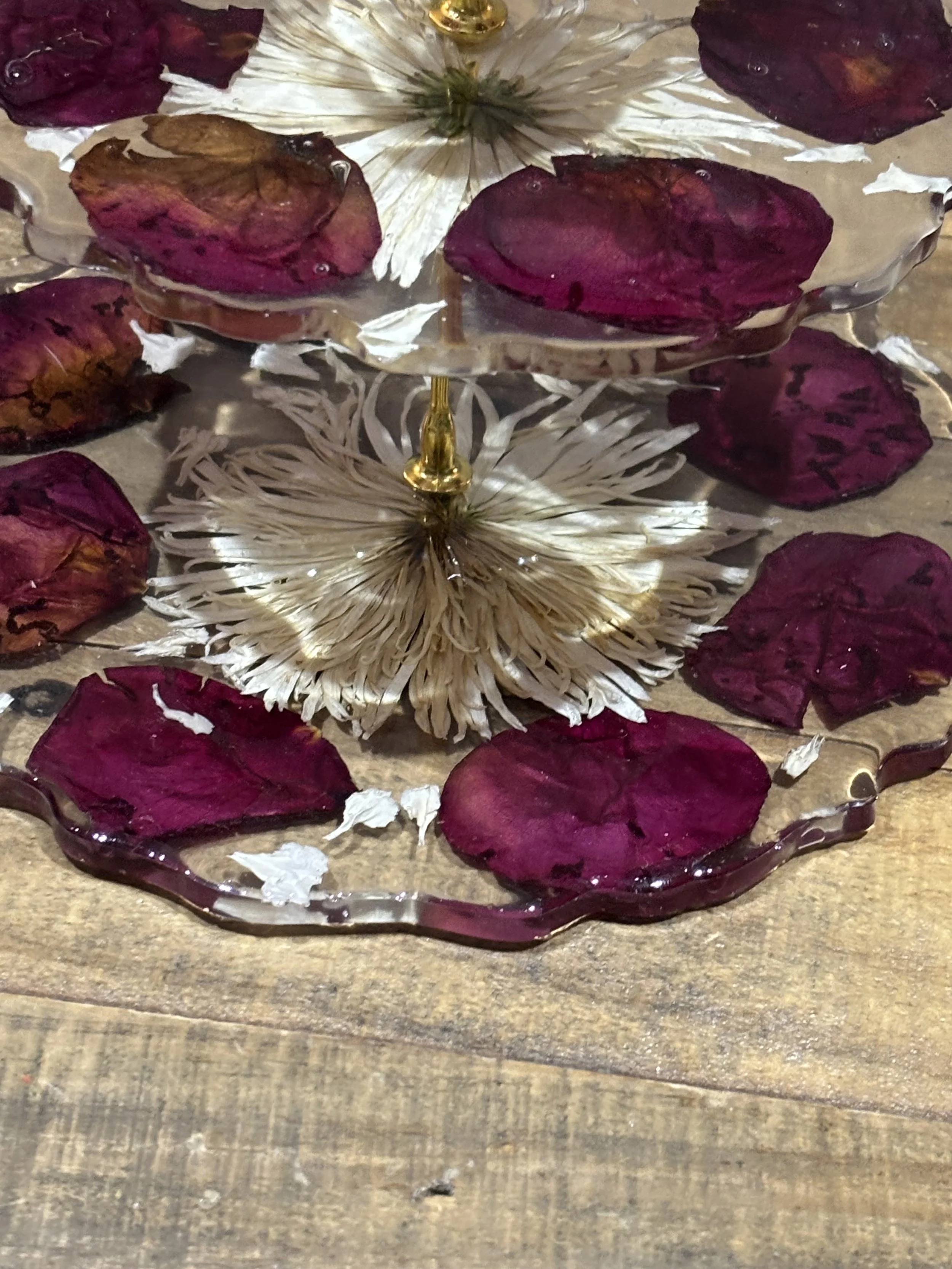 A glass dish with dried flower petals and flowers, resting on a wooden surface.