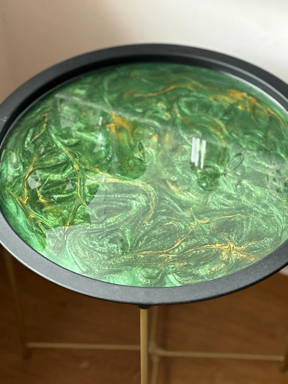A circular device with a swirling green and gold marbled pattern inside, covered by a transparent lid with a handle at the bottom center.