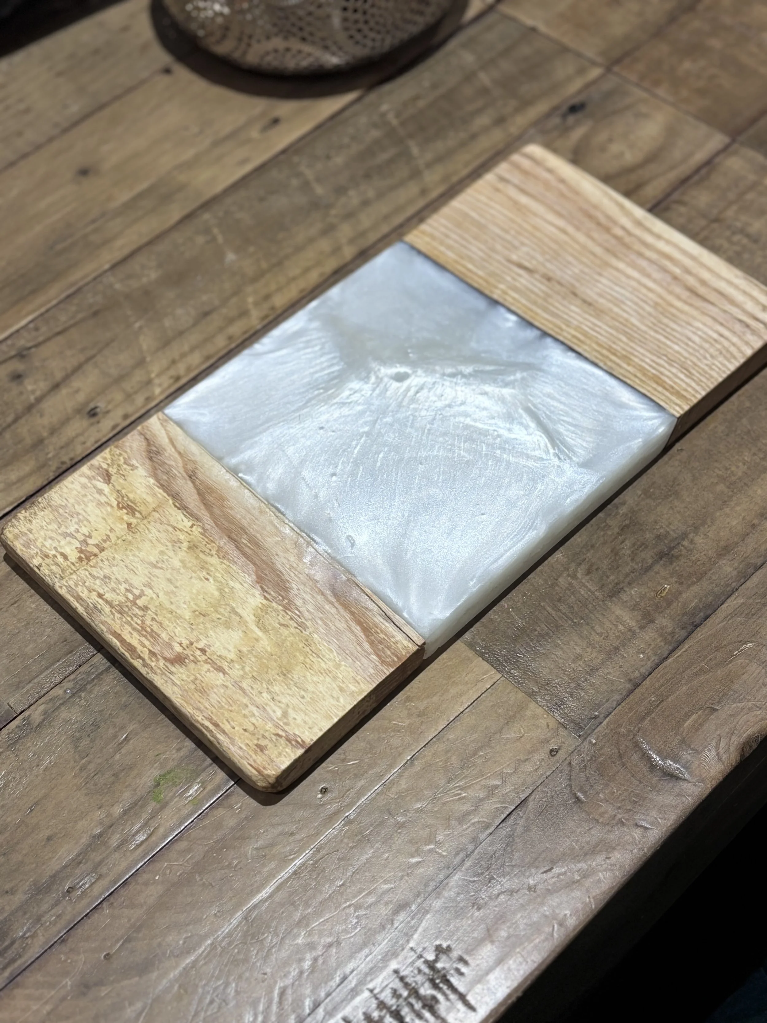 Wooden table with a recessed square opening in the center, framed with four wooden pieces, with a shiny, marbled material inside the opening.