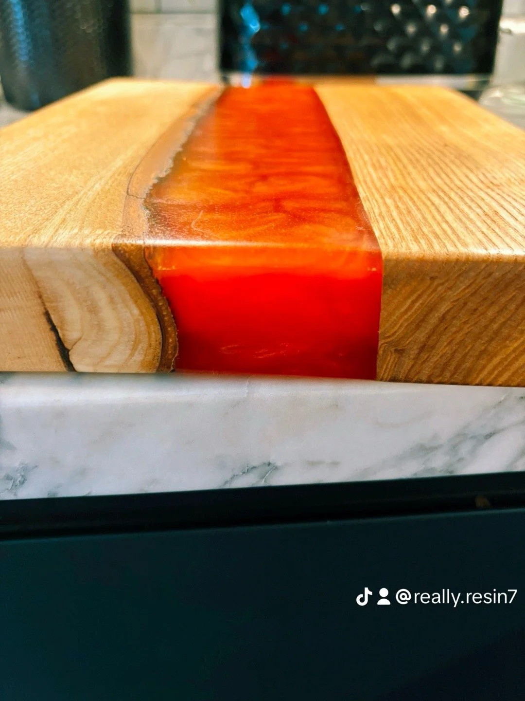 Close-up of a wooden block with a resin river running through the middle, showing the natural wood grain and a reddish-orange resin filling.