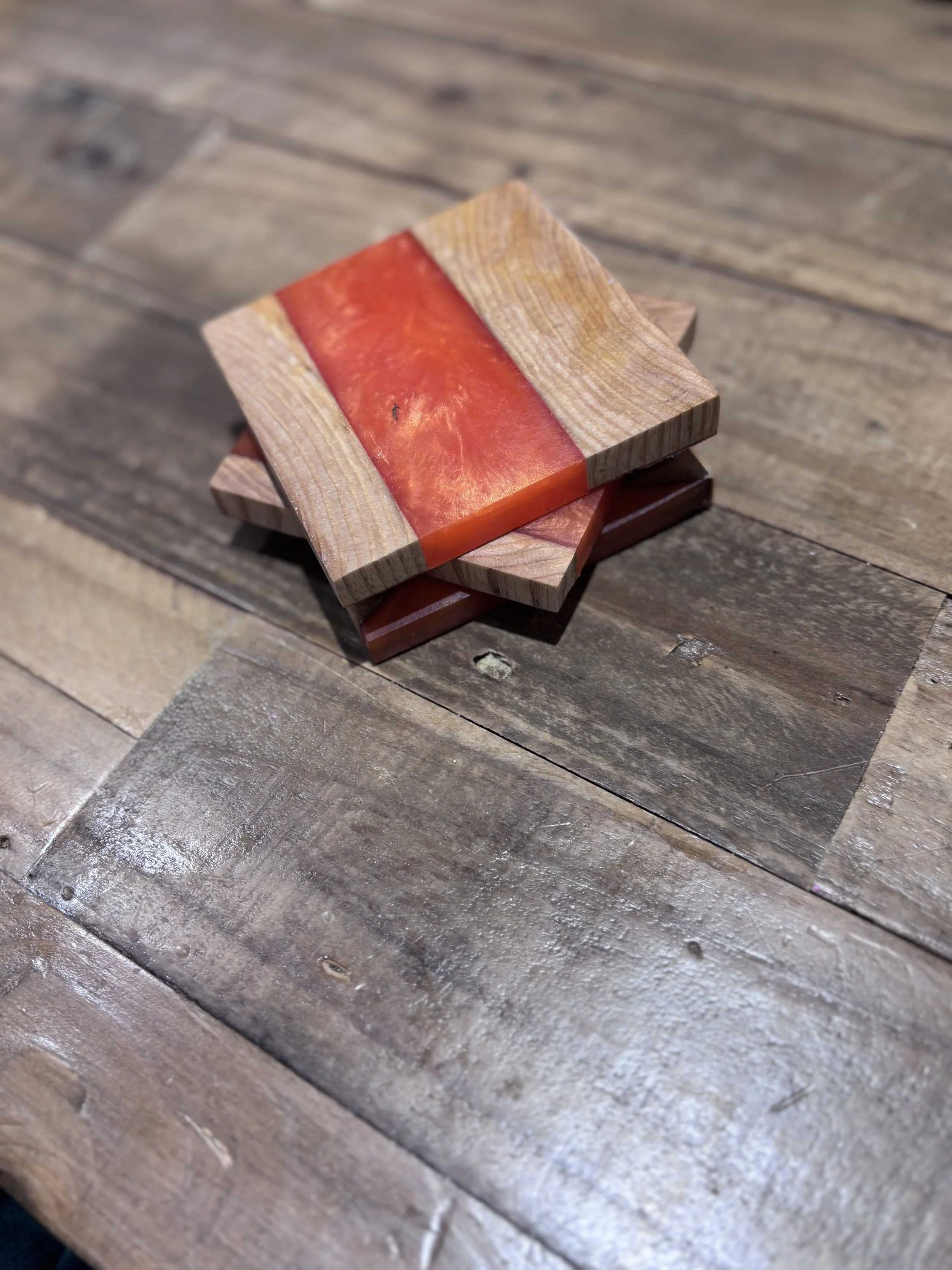 Three wooden coasters with orange and red resin inlays are stacked on a wooden surface.