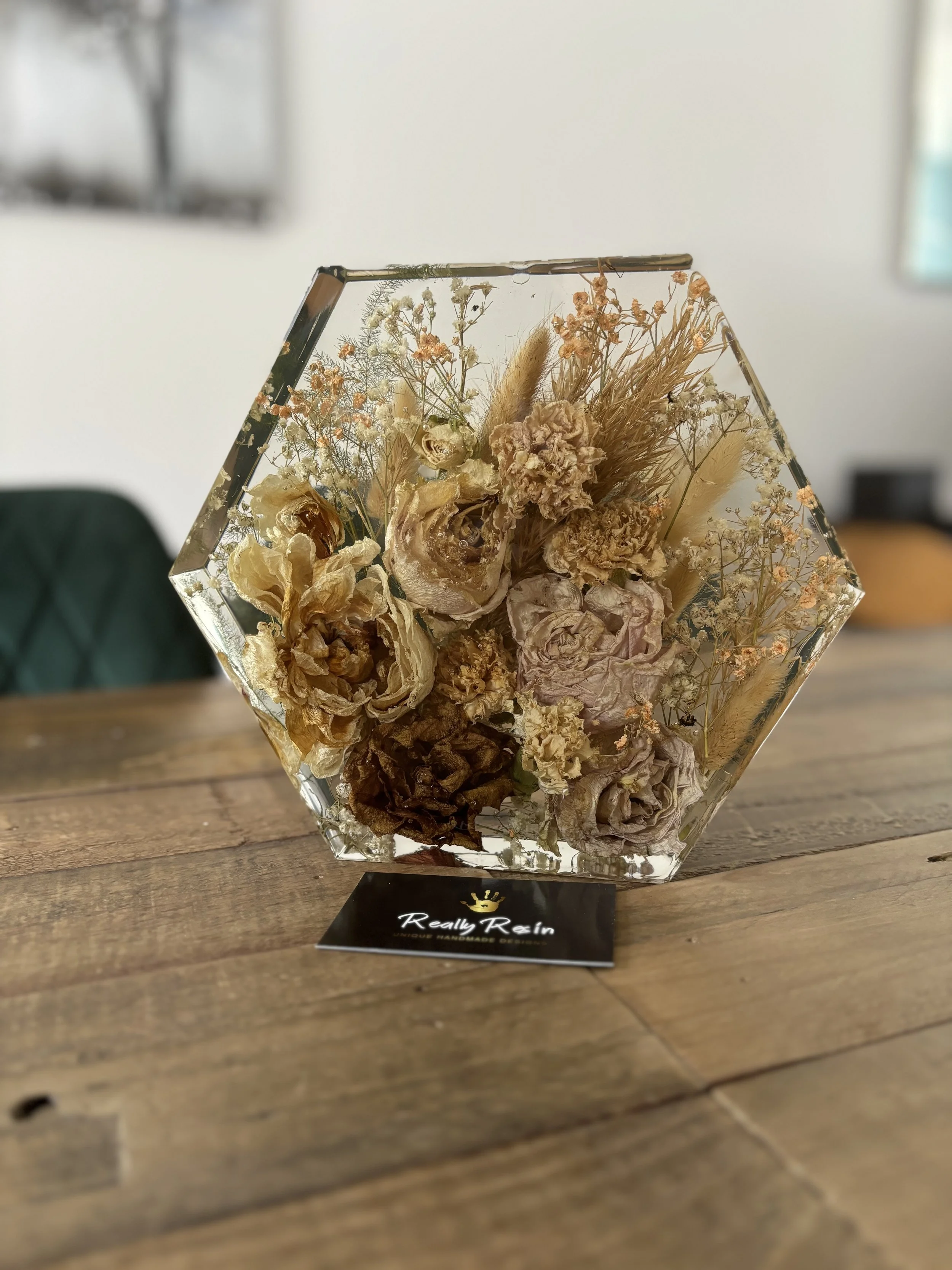 Decorative glass hexagon-shaped container filled with preserved dried flowers on a wooden surface.
