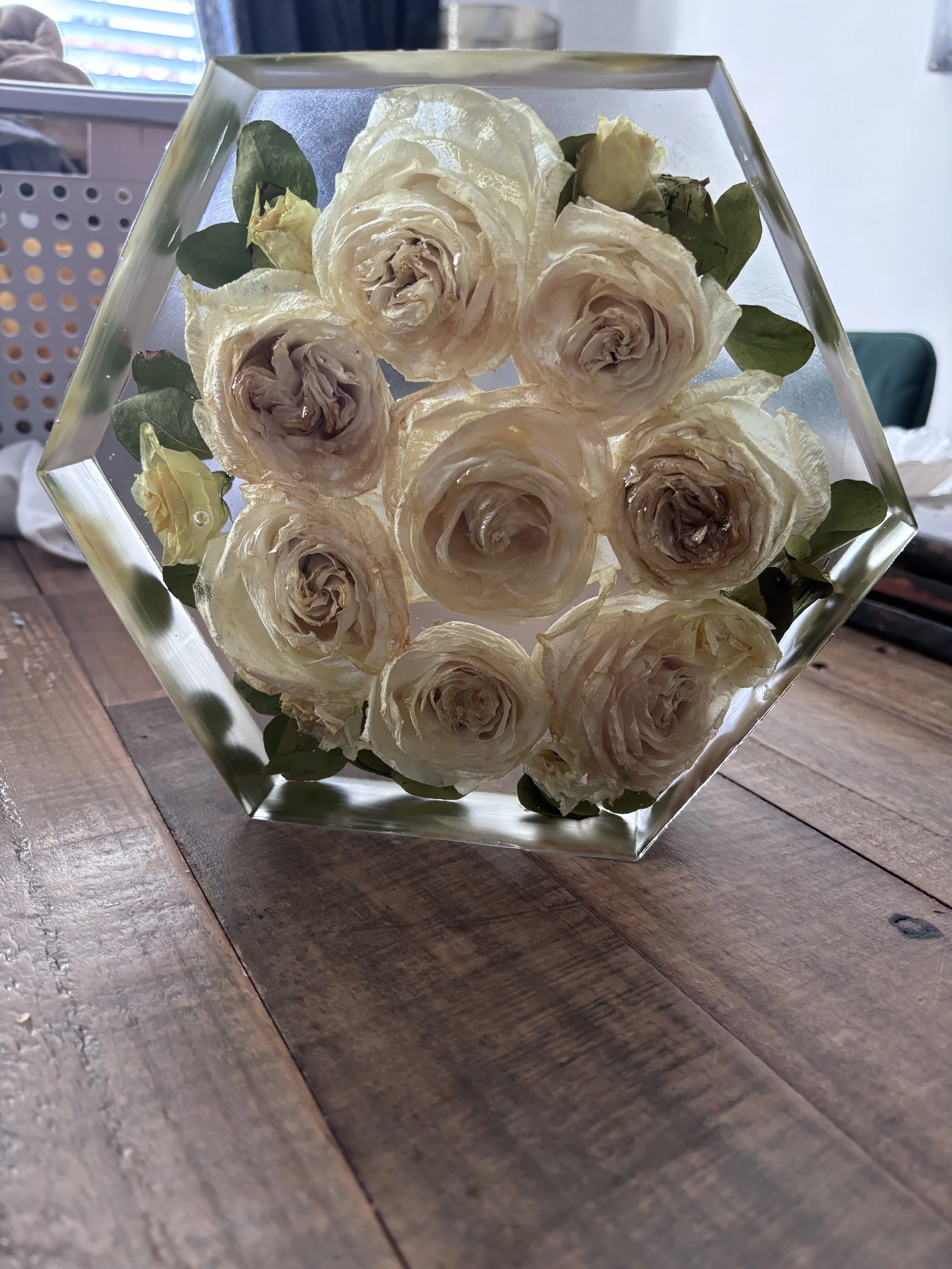 A glass hexagon-shaped vase filled with cream-colored roses, placed on a wooden table.