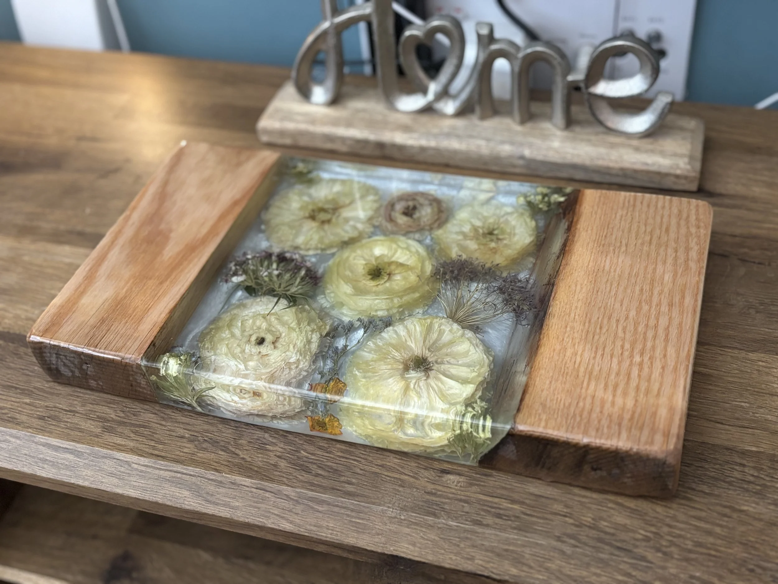 A wooden frame with flowers submerged in water, placed on a wooden table, with a decorative sign reading 'love' in the background.