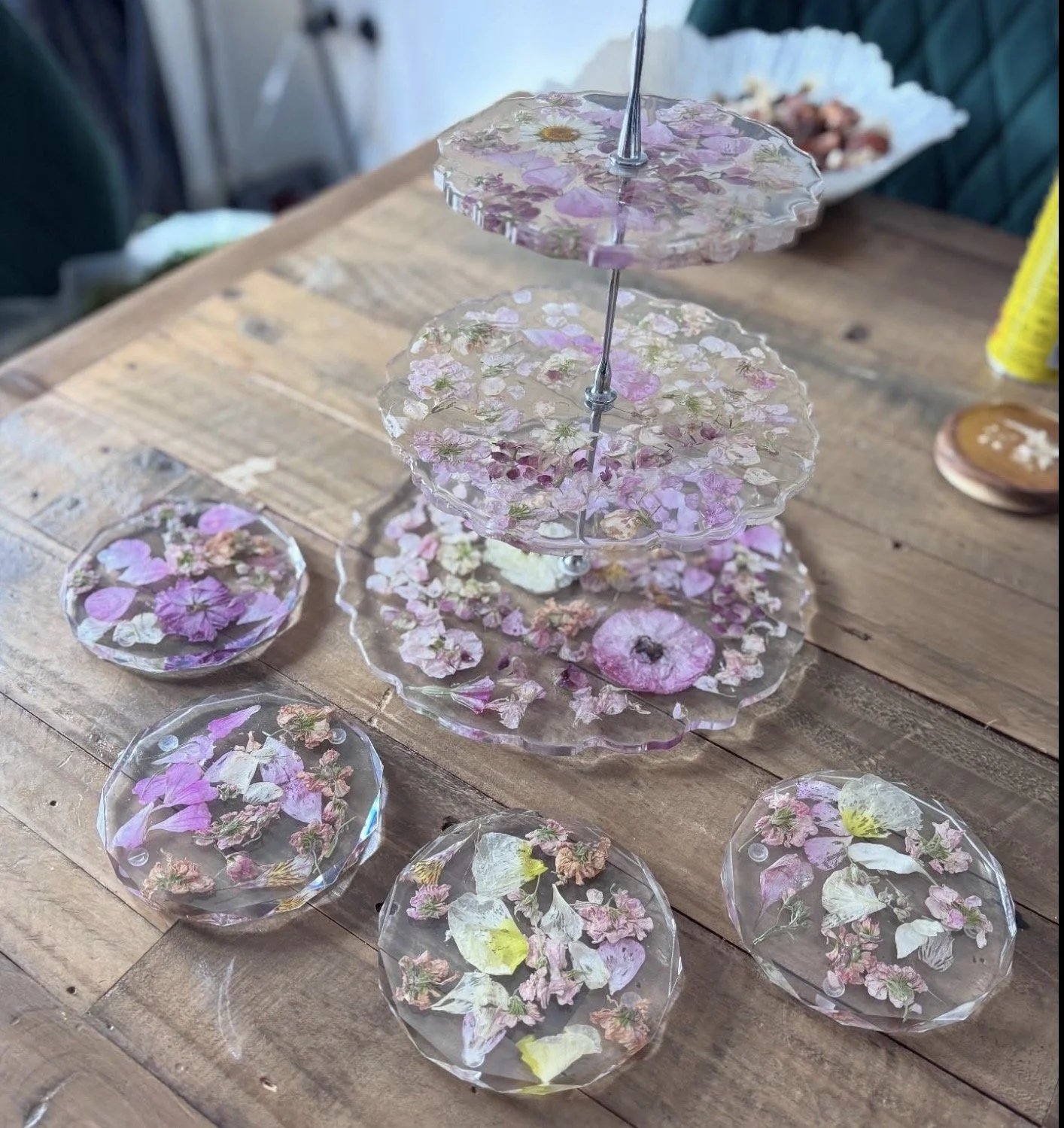 Decorative three-tiered plate stand and six small round plates with pressed flowers on a wooden table.