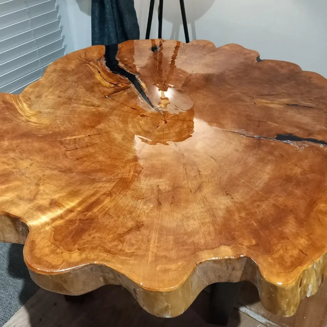 A close-up view of a polished wooden table with a natural, irregular shape and visible wood grain.