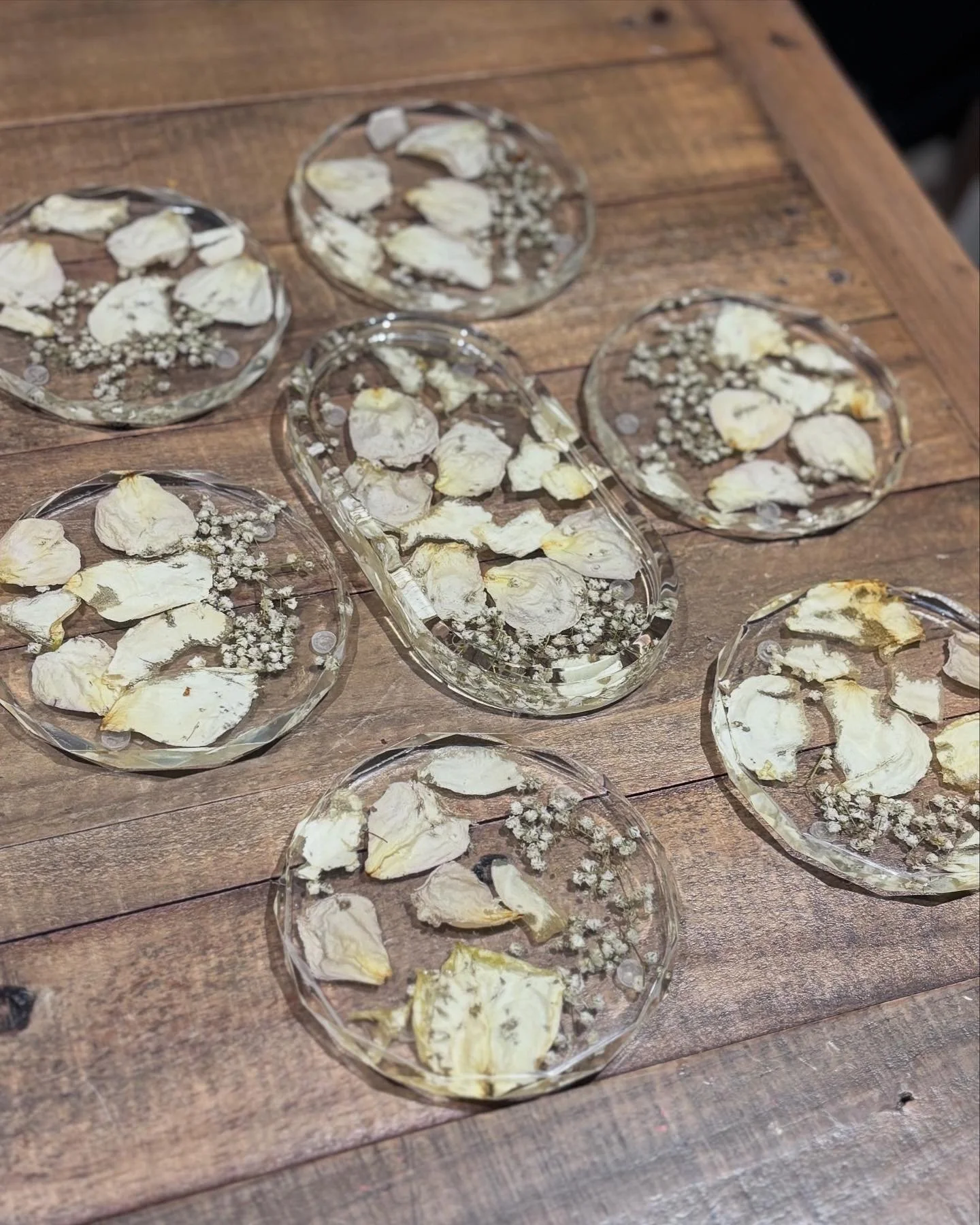 Several clear glass plates and trays with dried rose petals and small white flowers on a wooden table.