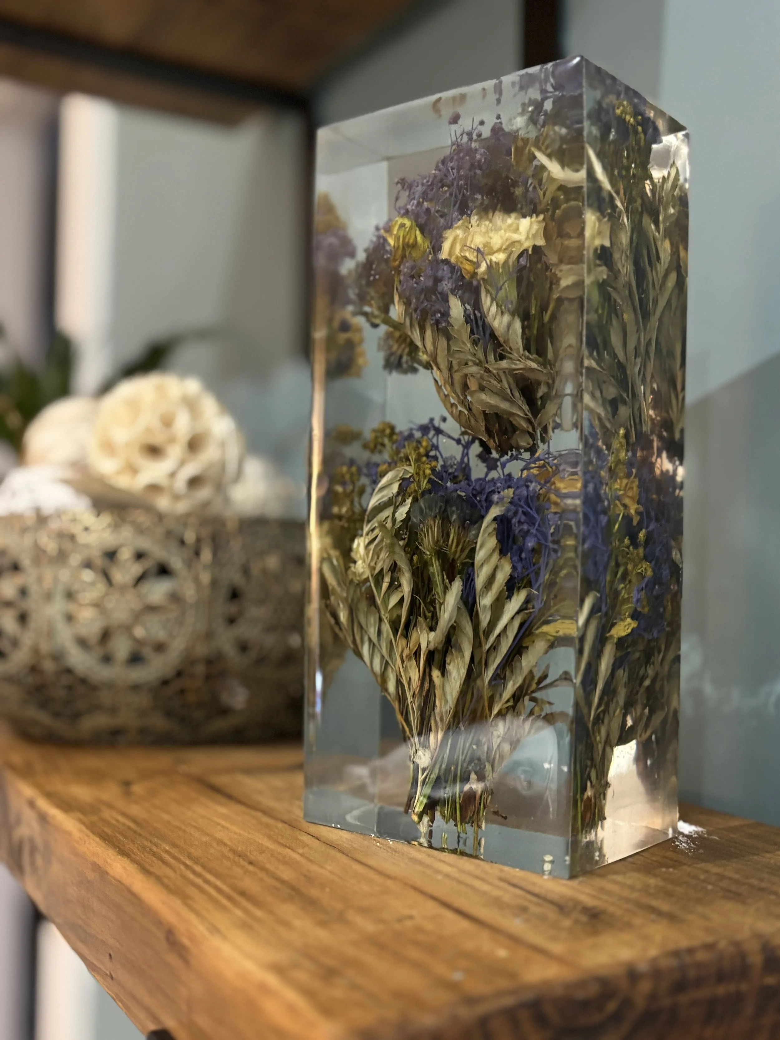 A rectangular clear resin block with preserved pressed flowers inside, placed on a wooden shelf.