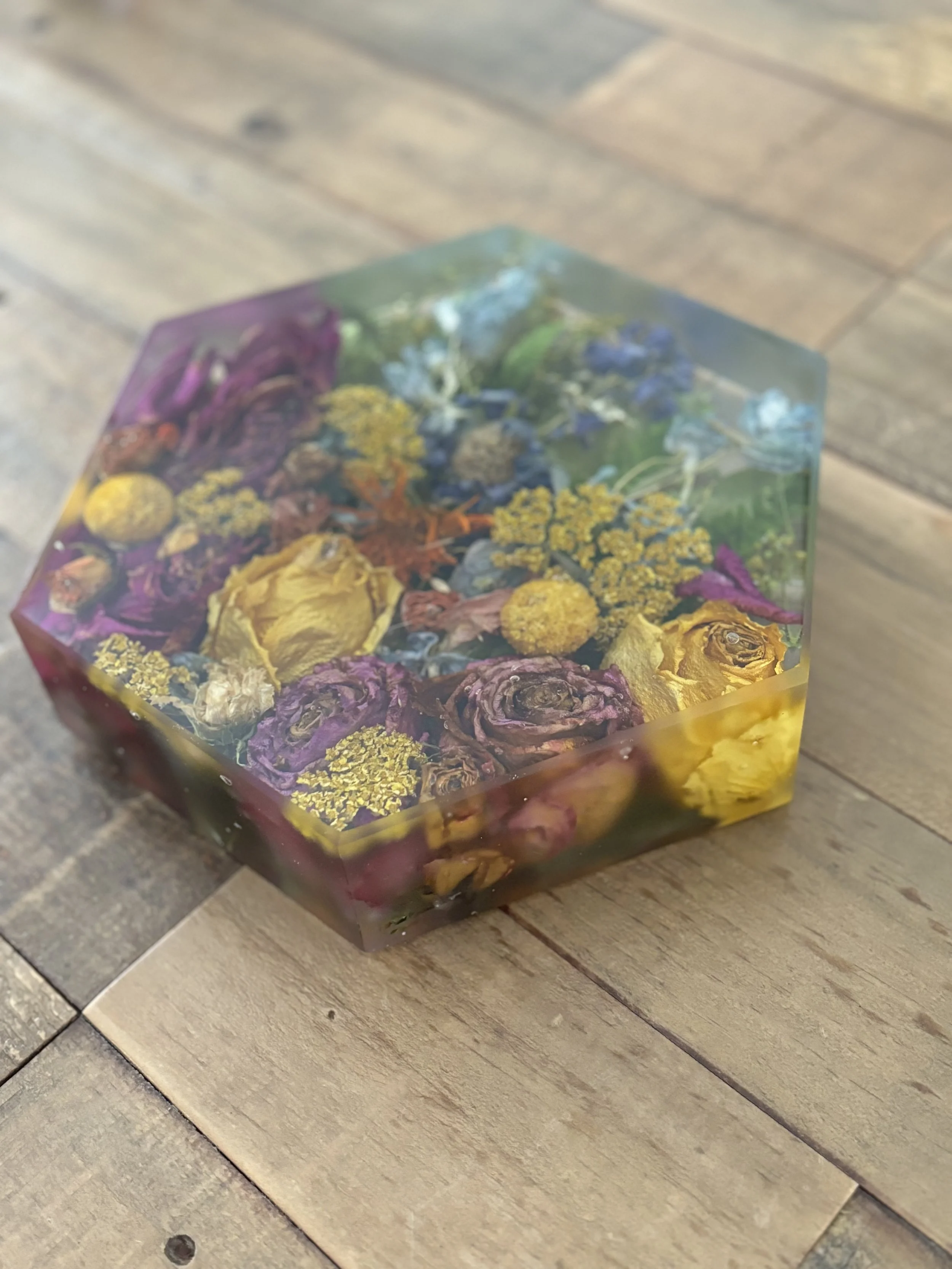 A rectangular resin art piece with embedded dried flowers and leaves, placed on a wooden surface.