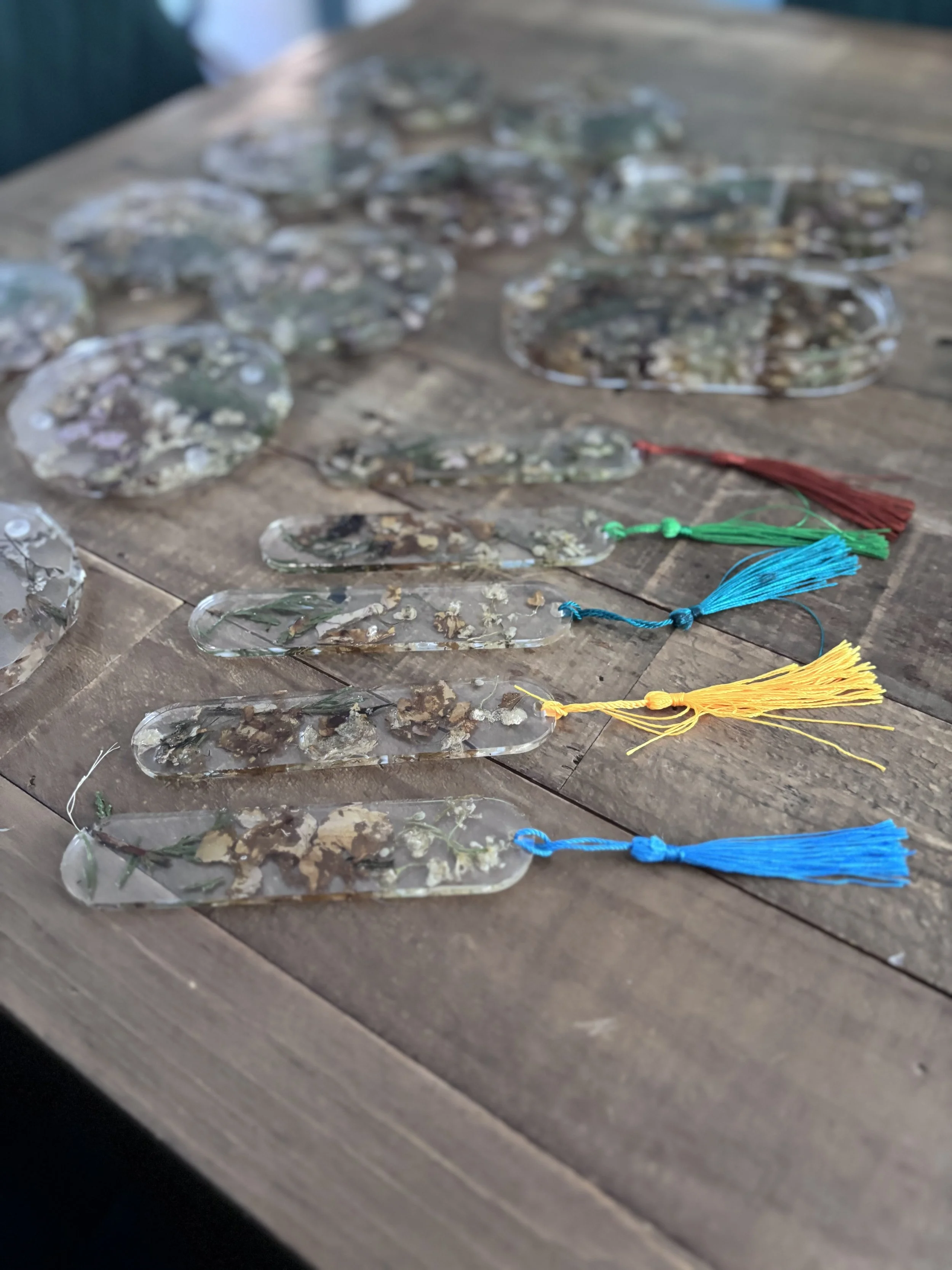 Multiple decorative glass pieces with dried flowers inside, each tied with colorful tassel cords in red, green, blue, and yellow, arranged on a wooden surface.