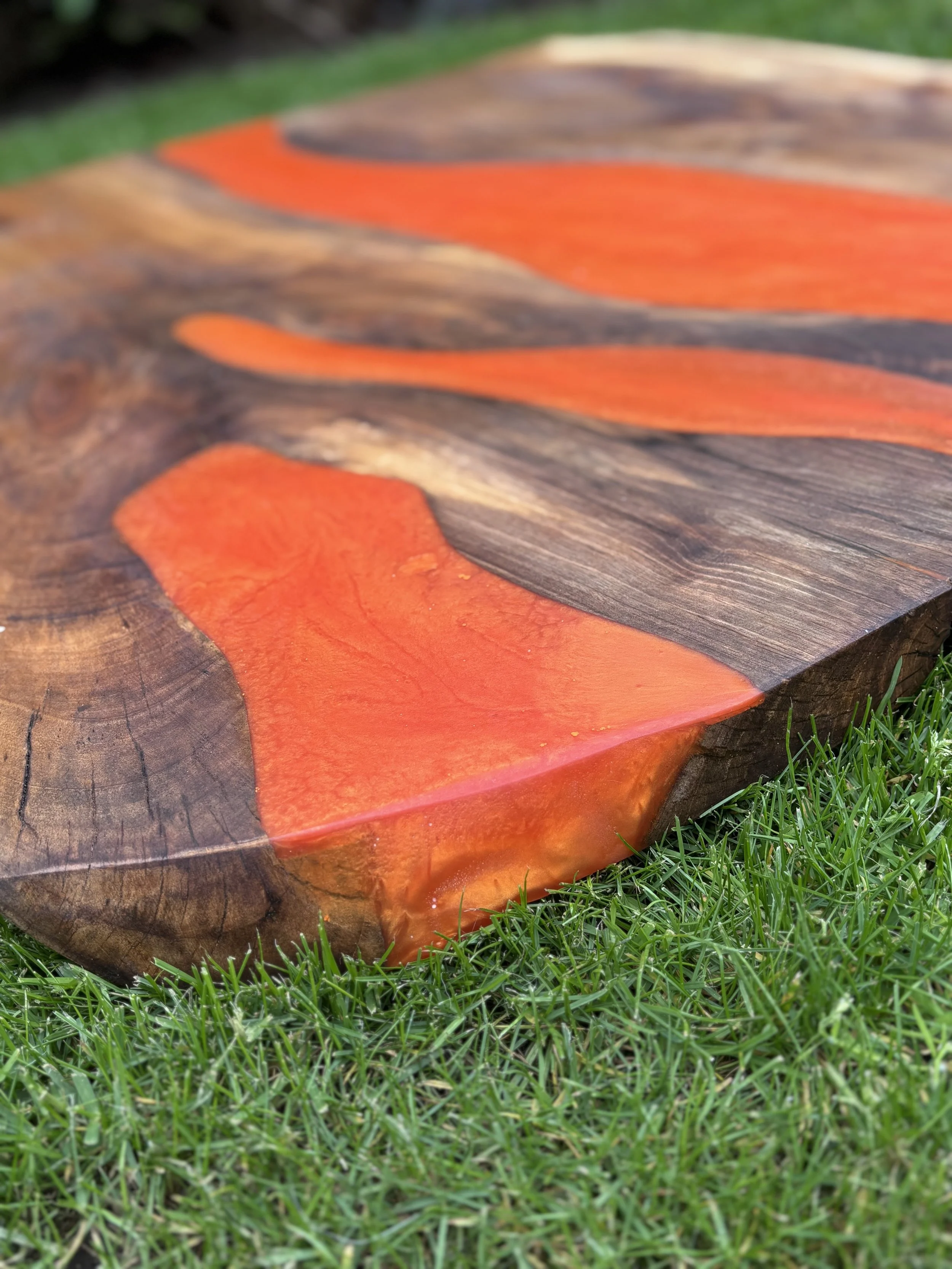 Close-up of a wooden table with orange and dark brown resin accents, placed on green grass.