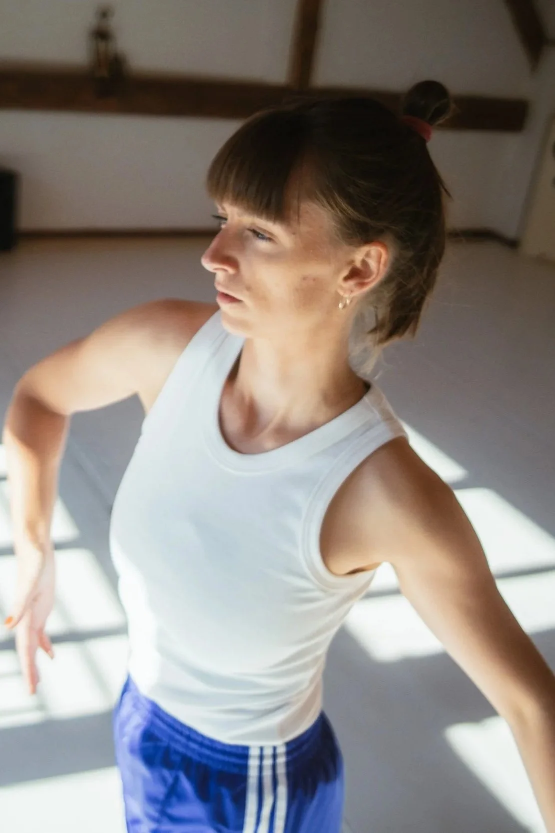 Junge Frau in sportlicher Kleidung macht offenbar Workout oder Yoga in einem Raum mit Dachbalken, Sonnenlicht ruht auf ihrem Gesicht und Arm.