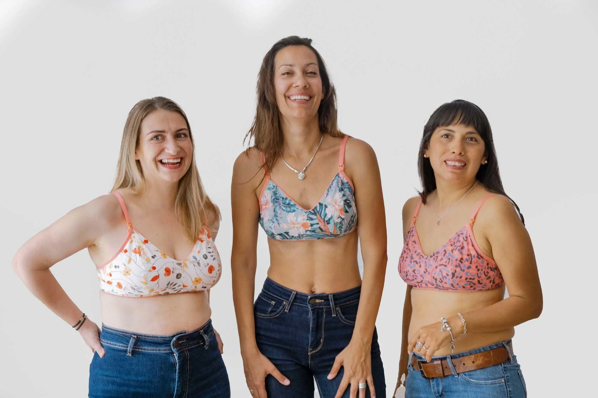 Tres mujeres sonriendo y vestidas con tops de ropa de baño o ropa de playa, de pie sobre fondo blanco.