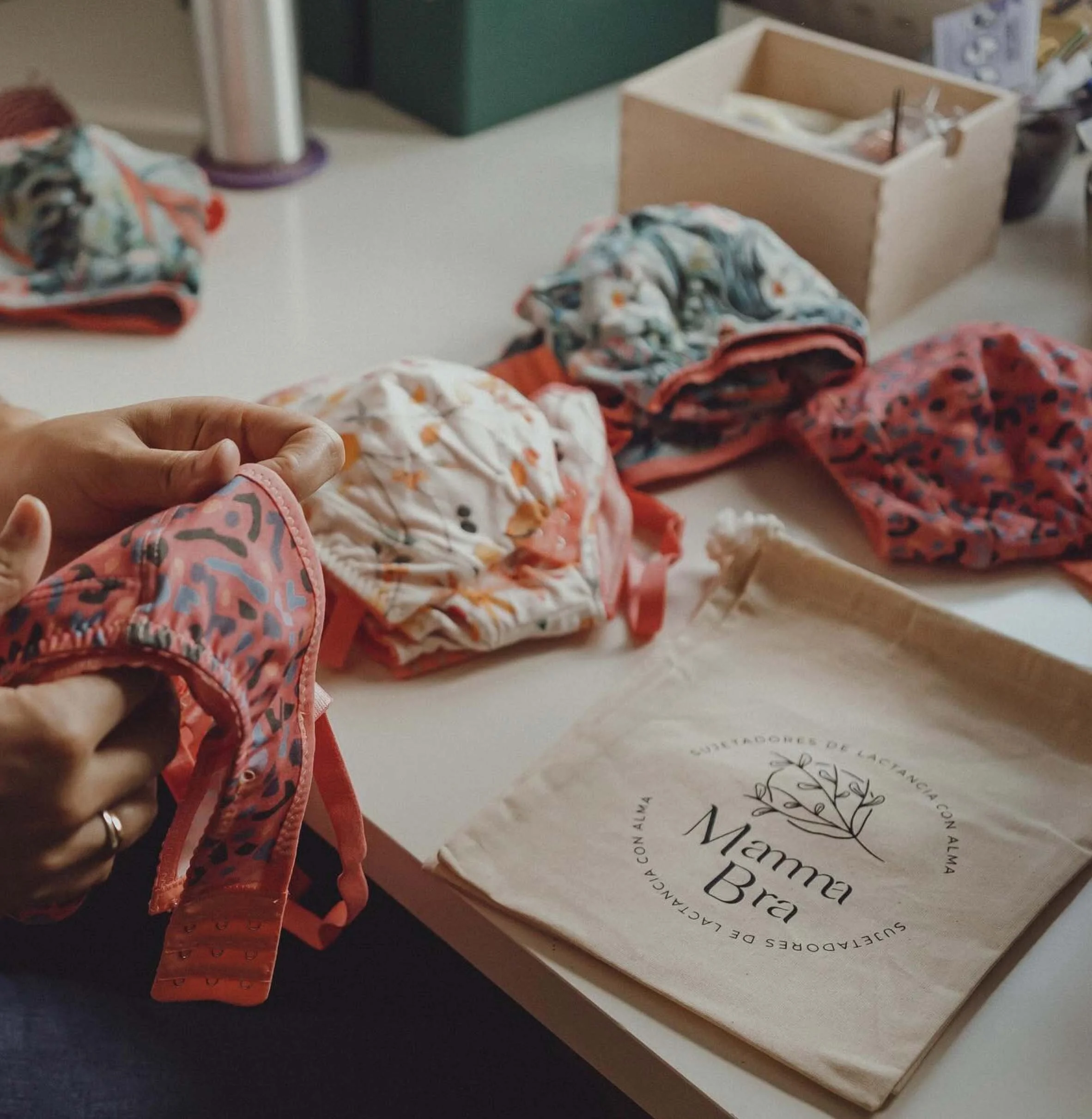 Mesa de trabajo con sujetadores de diversos estampados y bolsa de tela de Mamma Bra.